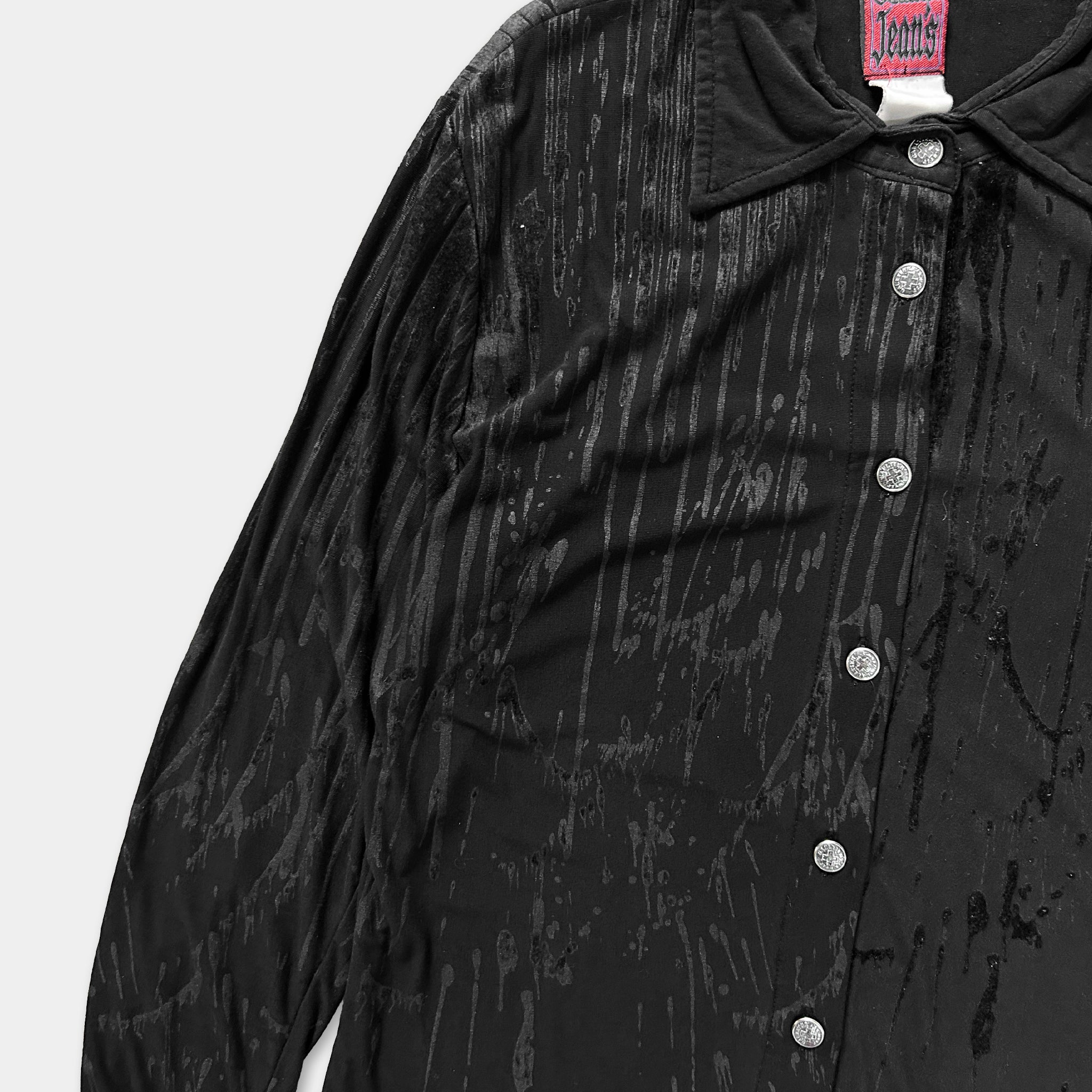 A close-up view of a black, long-sleeved shirt with a collar and buttons, featuring a textured, shiny appearance.