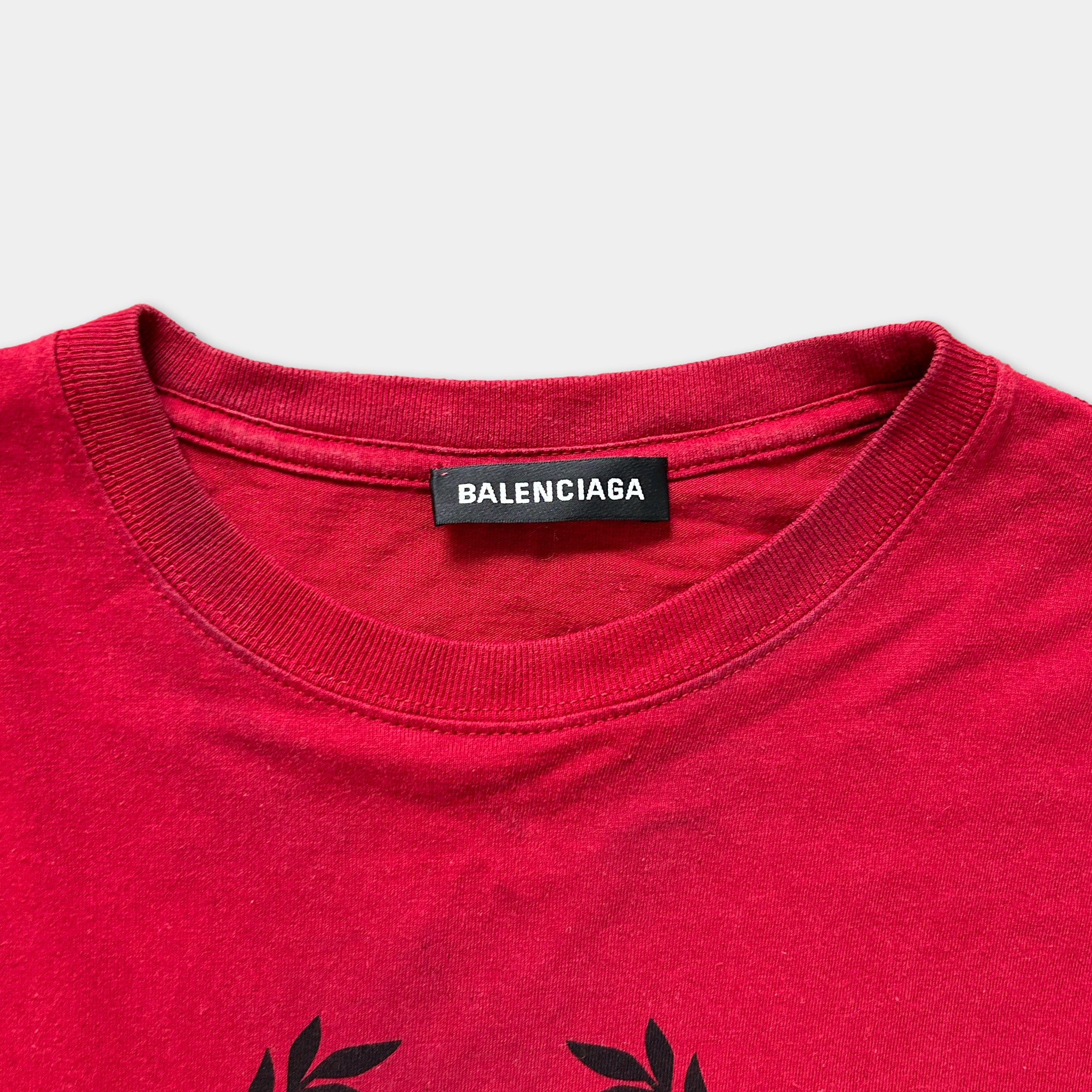 A red t-shirt with a Balenciaga logo and a black label on the collar.