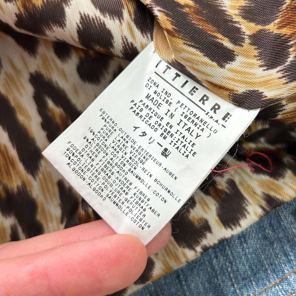A close-up of a hand holding a label with text on it, against a leopard print background.