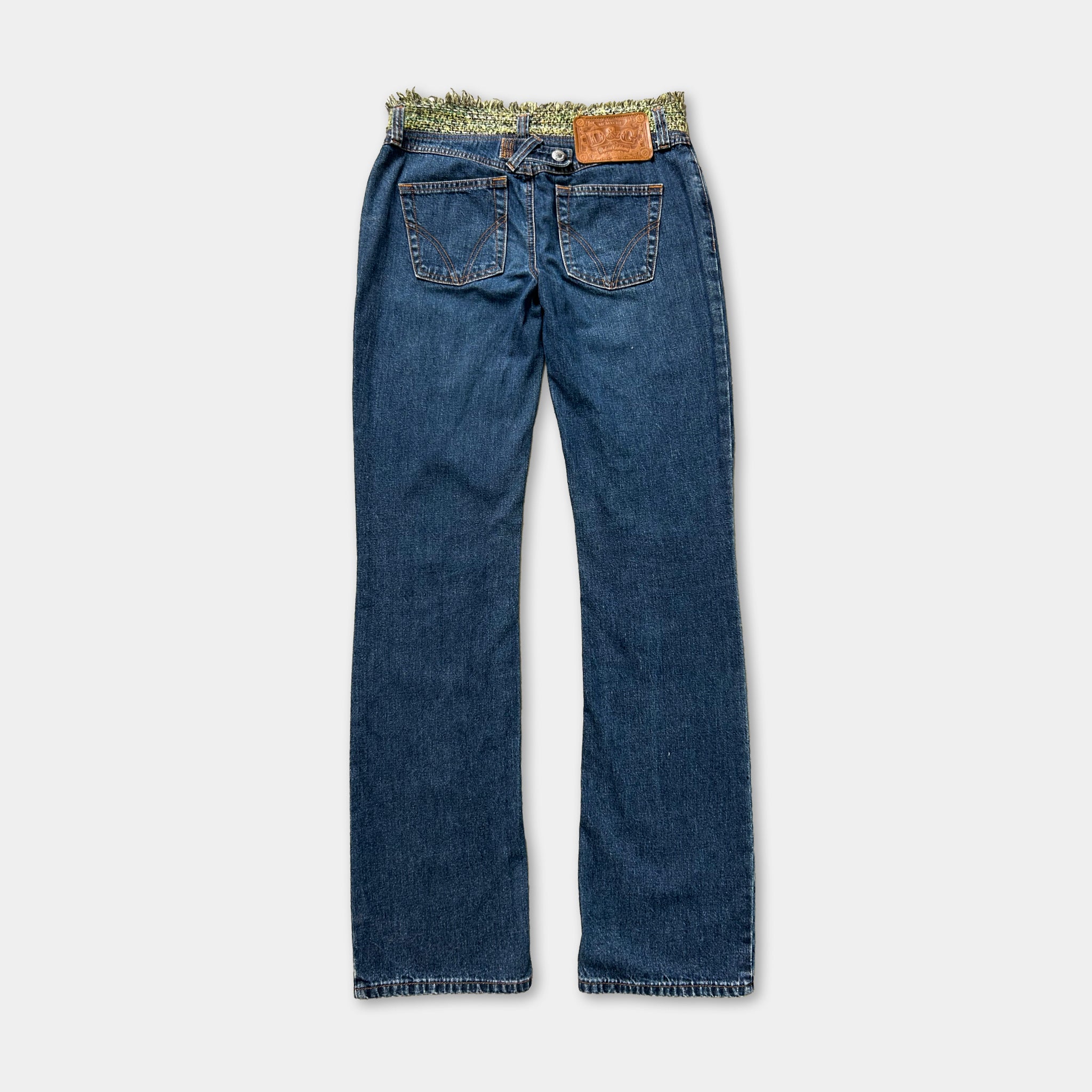 A pair of blue jeans with a patterned belt and a small leather patch on the waistband.