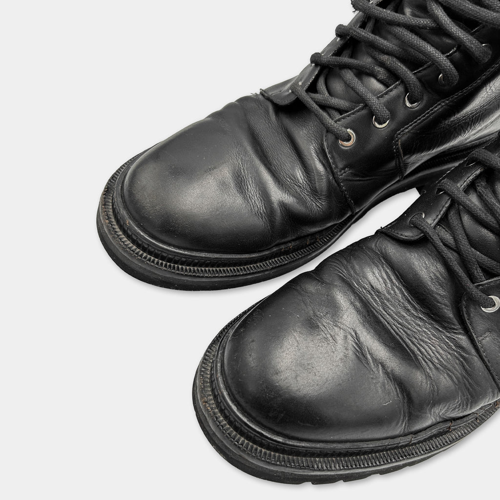 A close-up view of a pair of black leather boots with laces and soles visible.