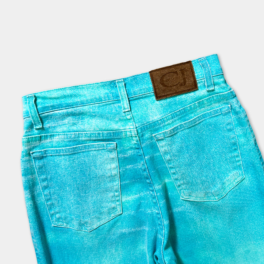 A pair of turquoise-colored jeans with a brown leather patch on the back pocket.