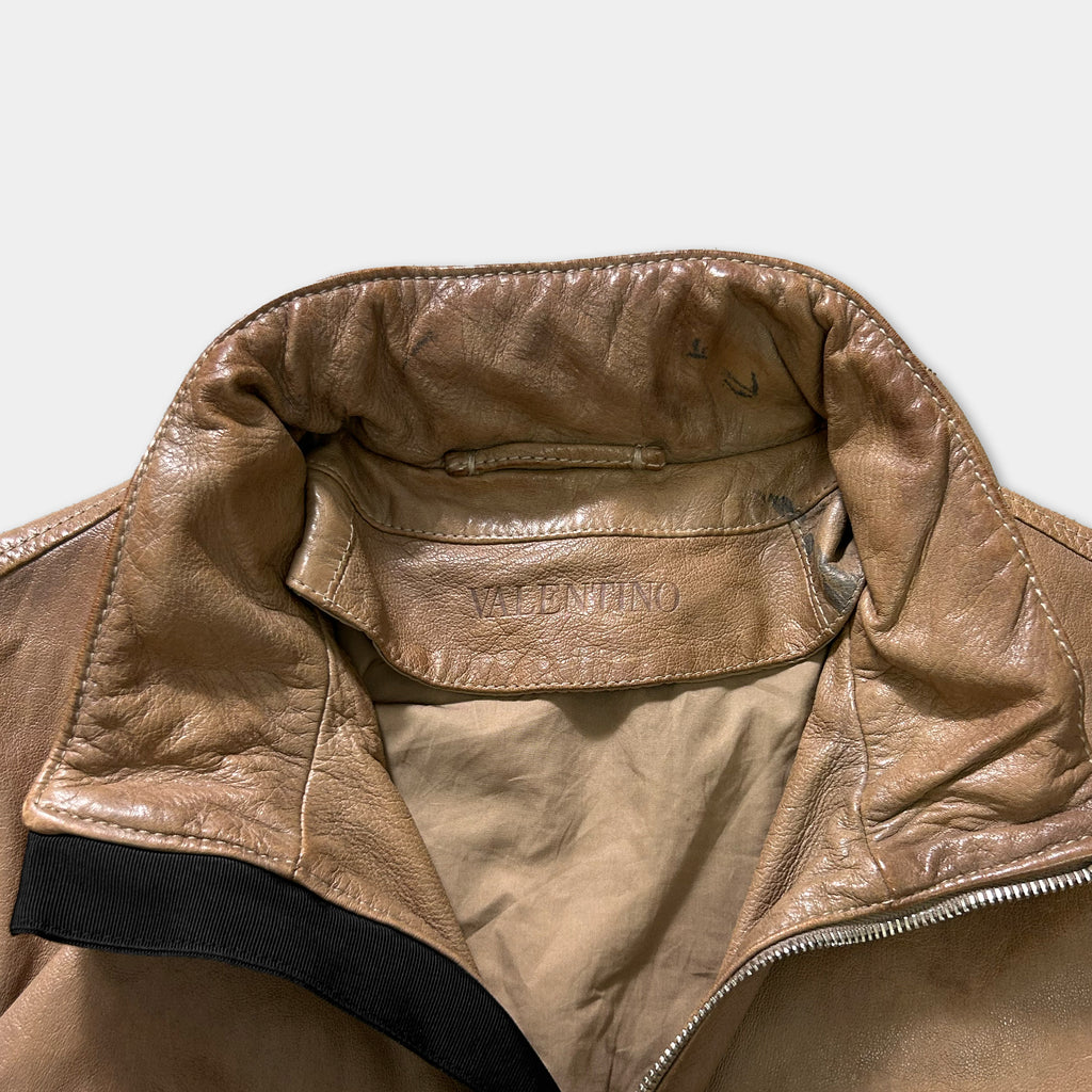 A close-up view of a tan leather jacket with a black zipper and a label on the collar.