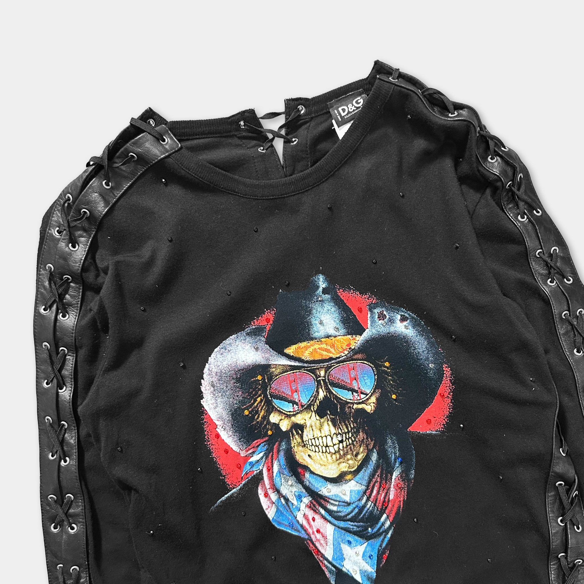 A black shirt with a graphic design featuring a skull wearing sunglasses and a cowboy hat, along with a red and blue scarf.