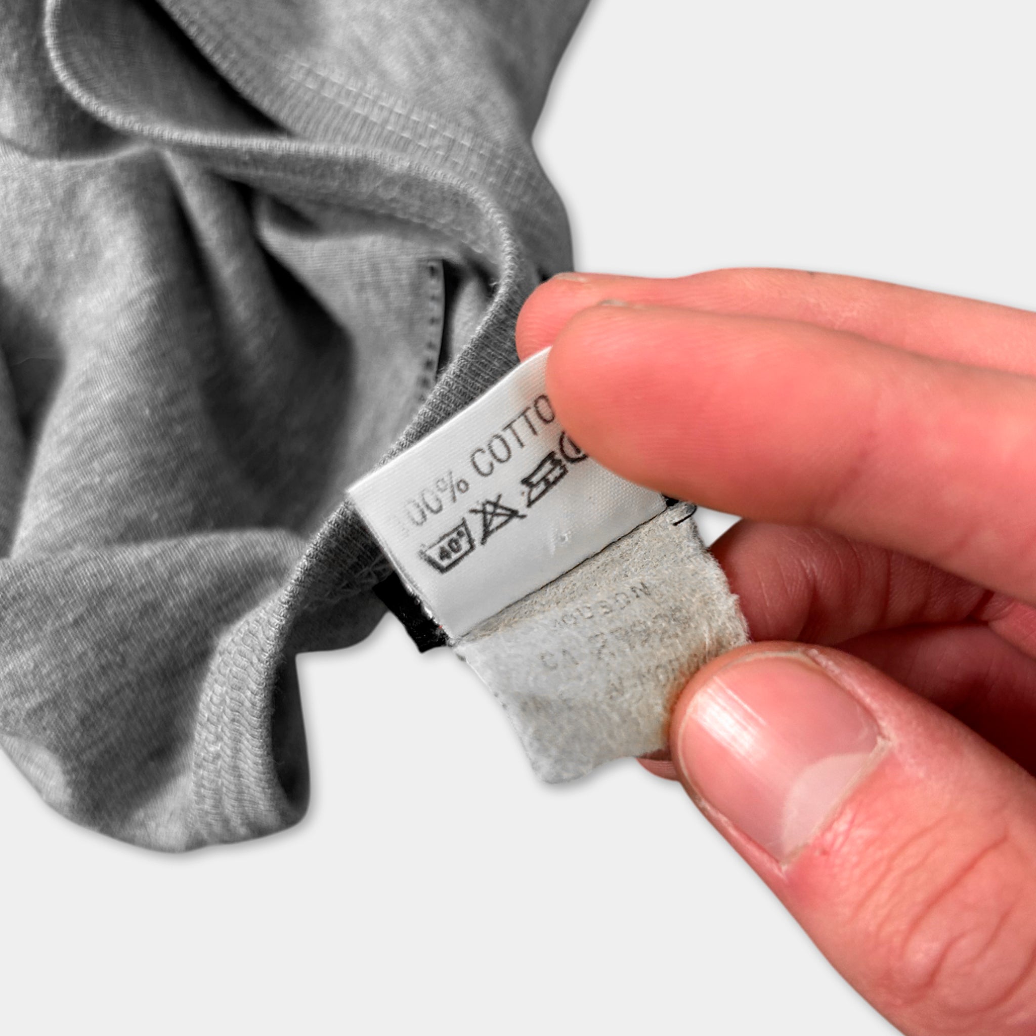 A person's hand holding a white label with text and symbols, against a gray background.