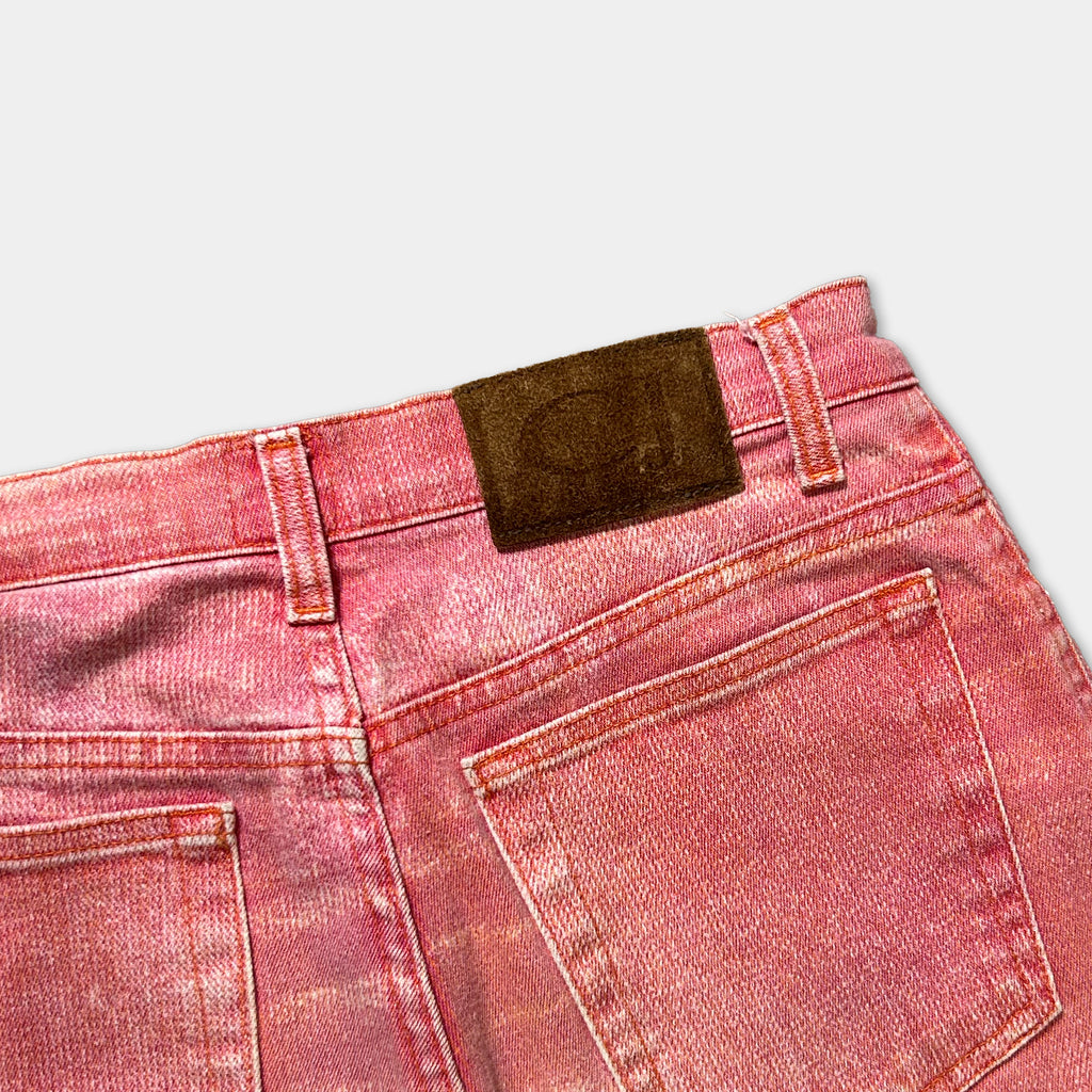 A close-up view of a pair of red denim jeans with a brown leather patch on the waistband.
