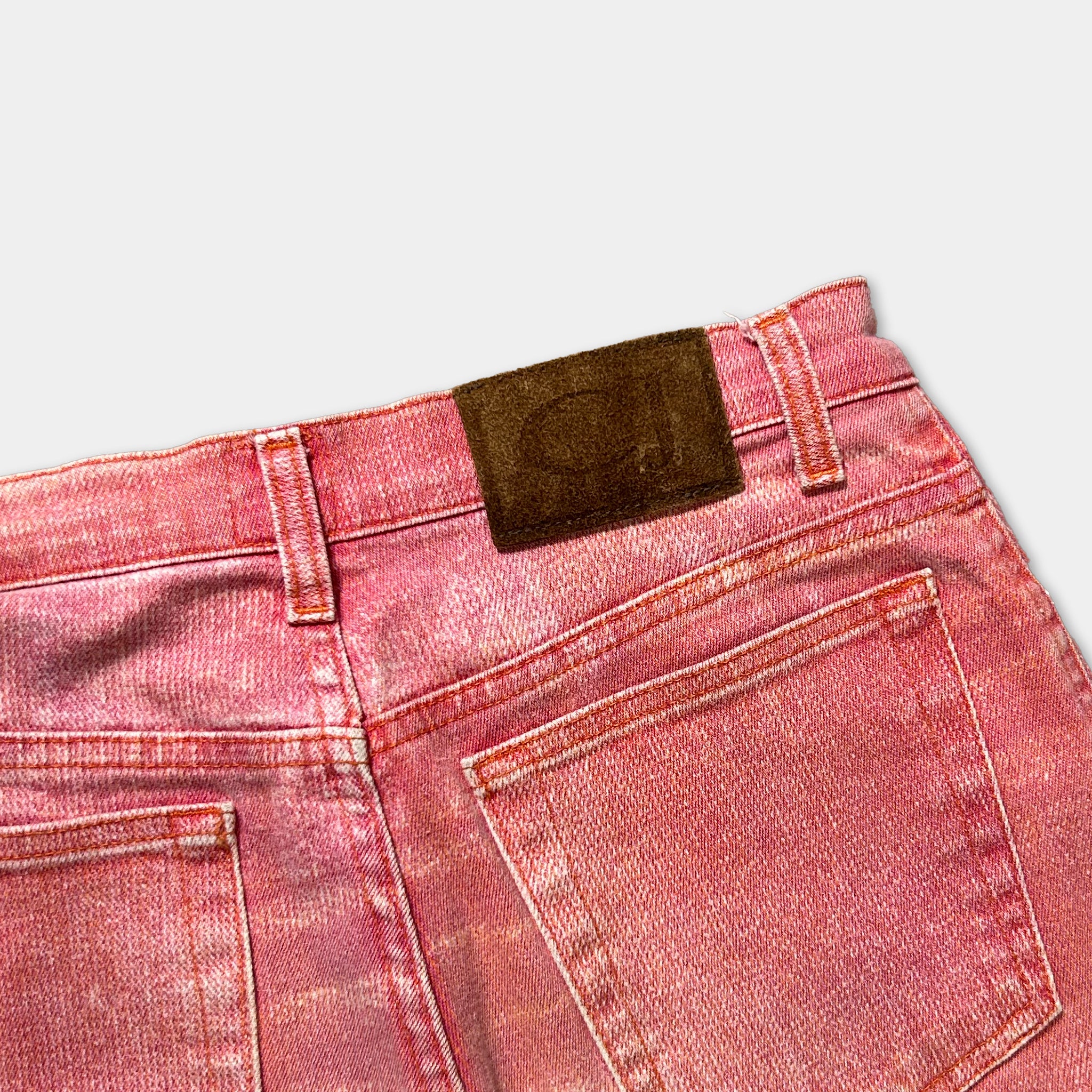 A close-up view of a pair of red denim jeans with a brown leather patch on the waistband.