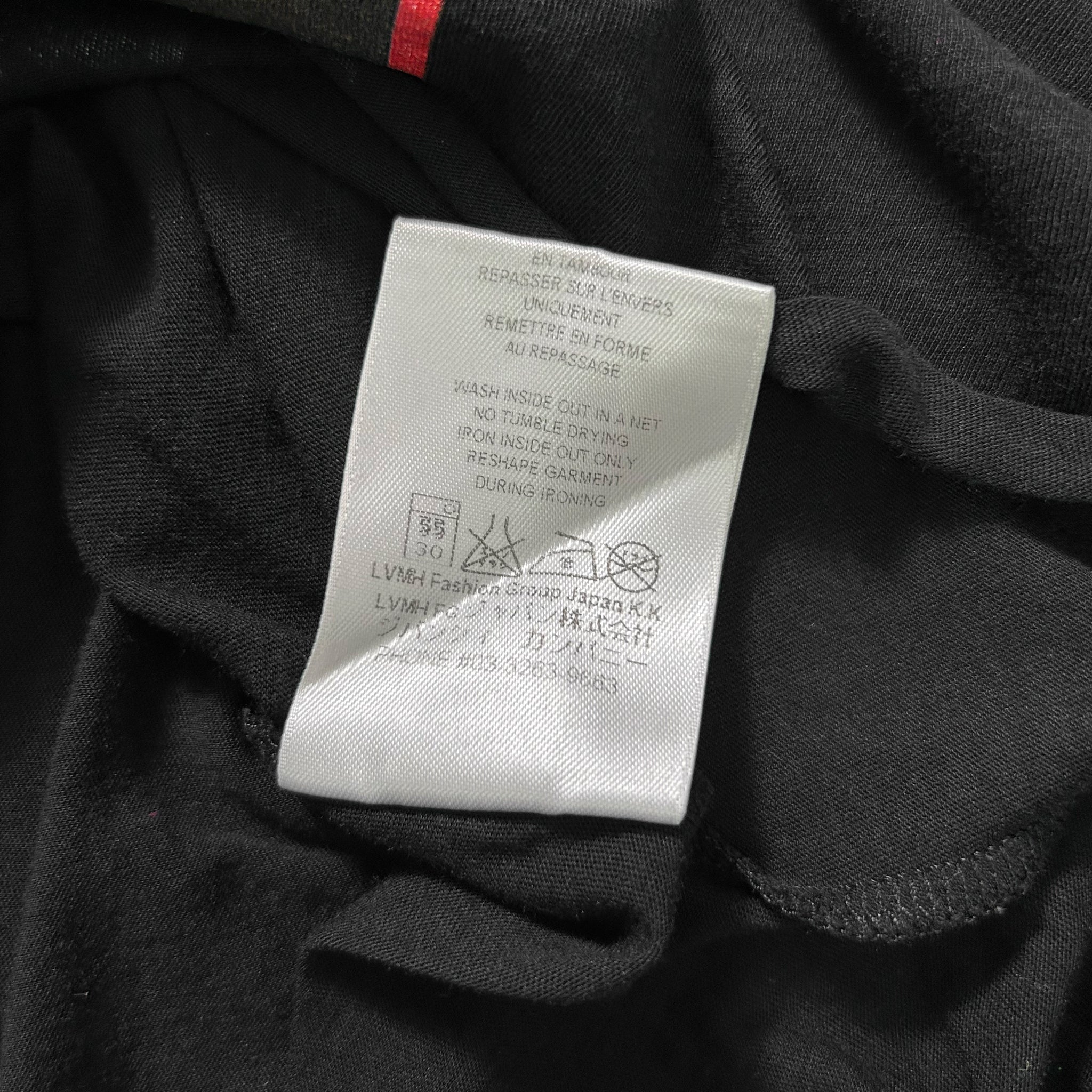 a close-up view of a black fabric, possibly a garment or textile, with a white label attached to it. The label contains text and instructions related to the product, such as washing and drying care.