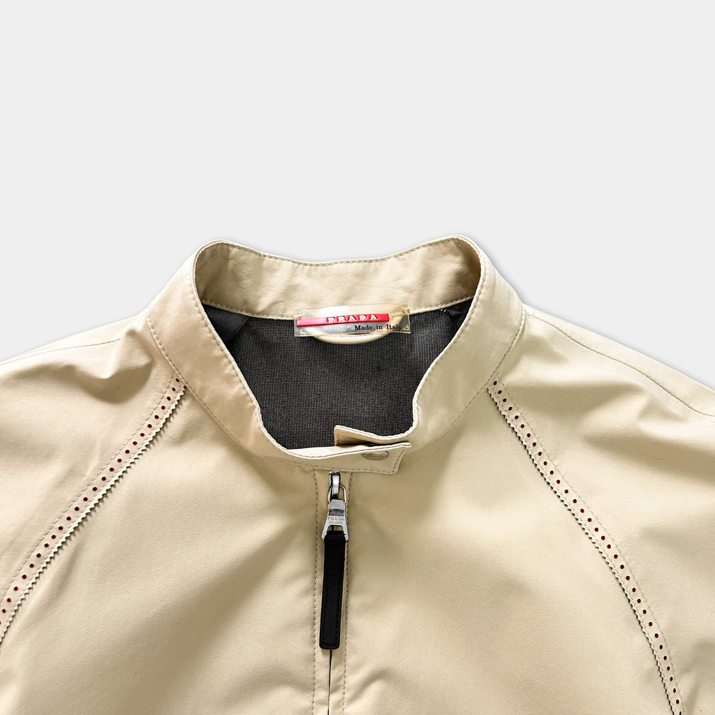 A beige jacket with a black collar and zipper, featuring a red label on the collar.
