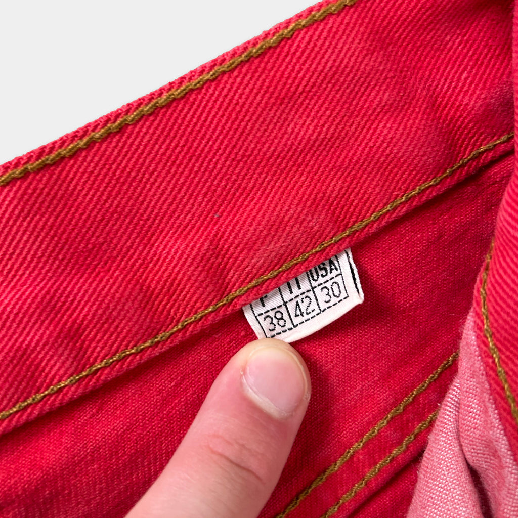 A close-up view of a red fabric, possibly denim, with a label attached to it. The label appears to contain text and numbers, but the specific details are not clearly visible.