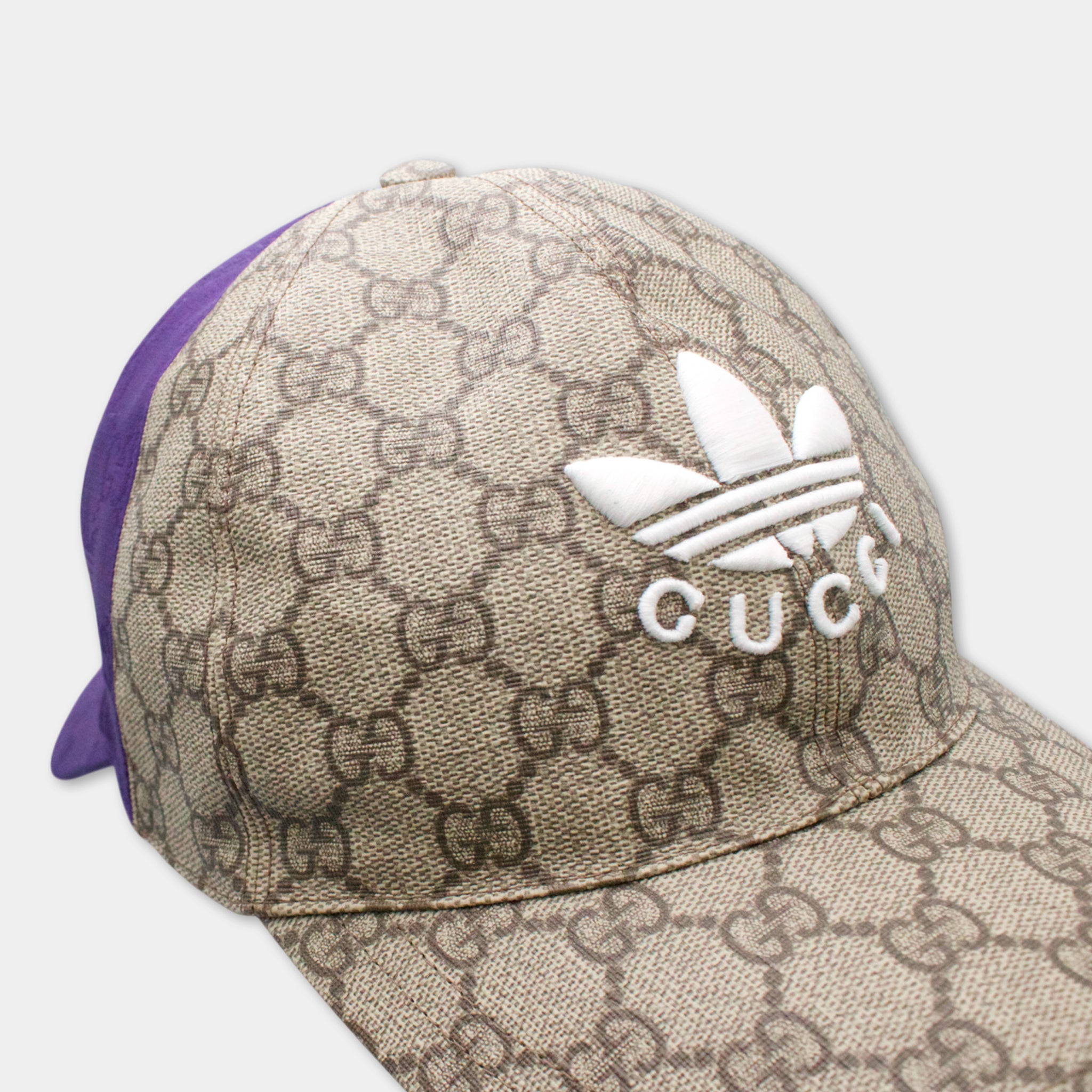 A close-up view of a Gucci-patterned baseball cap with the Adidas logo.