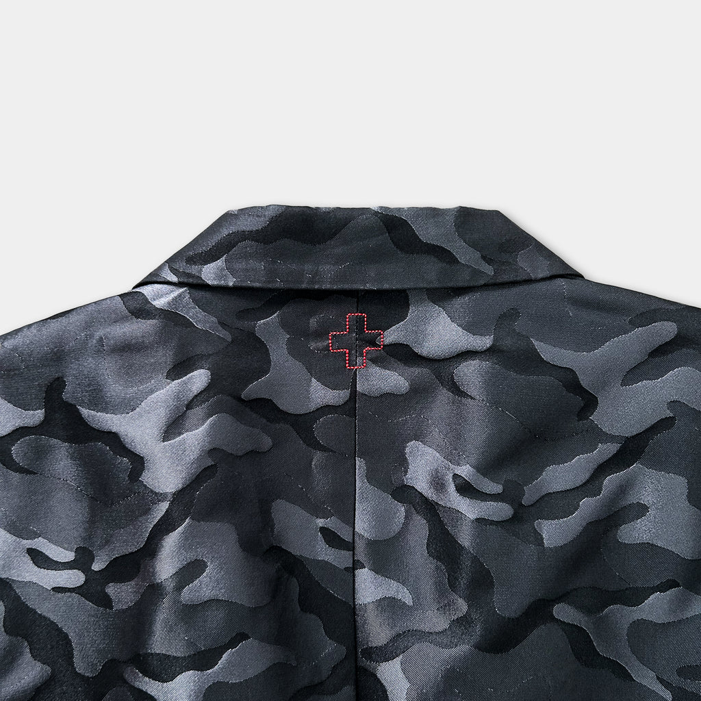 the back of a black and gray camouflage jacket with a red cross embroidered on the collar.