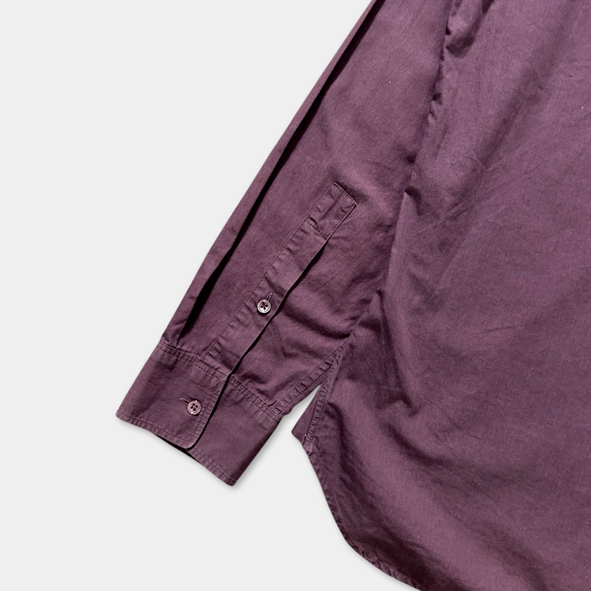 A close-up view of a purple shirt with a button and a pocket on the sleeve.