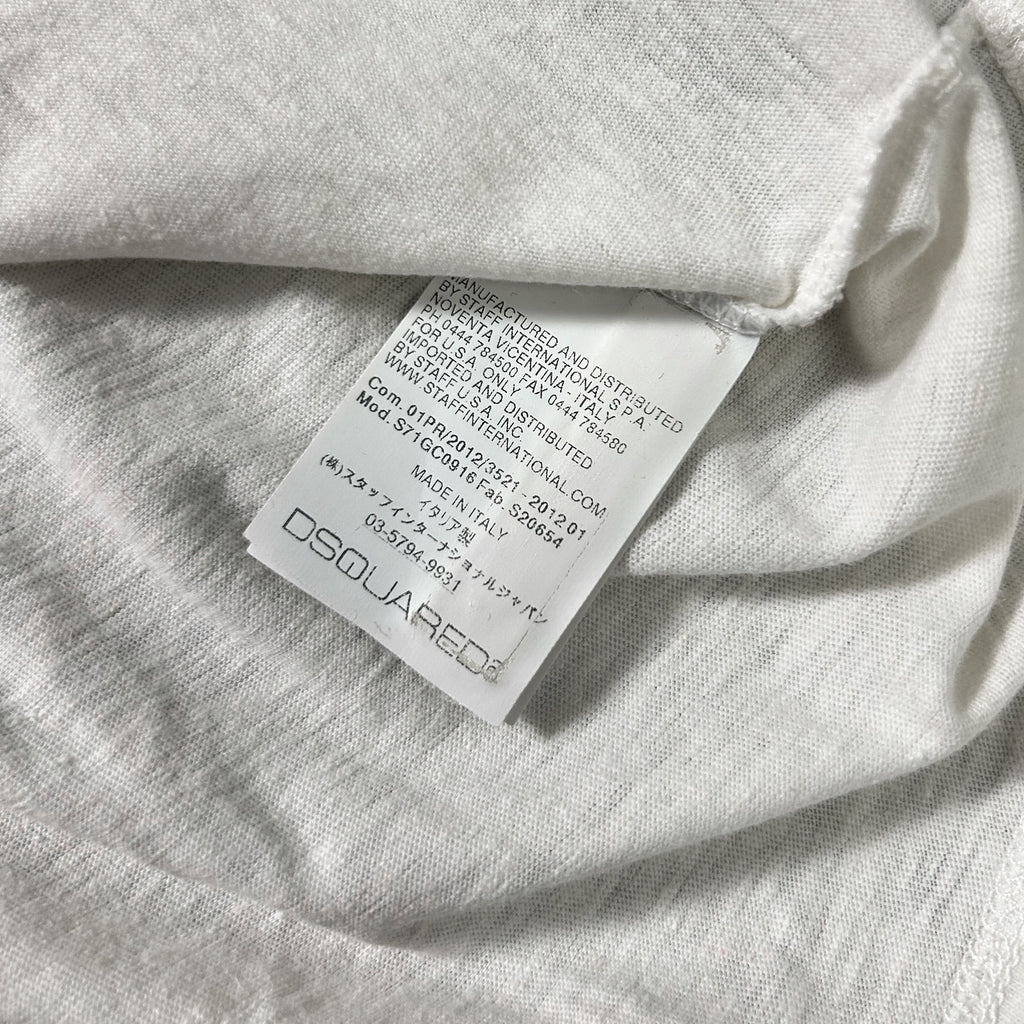 a close-up view of a white fabric, possibly a piece of clothing, with a label attached to it. The label appears to be a tag or label from a clothing brand, and it contains text in a foreign language.