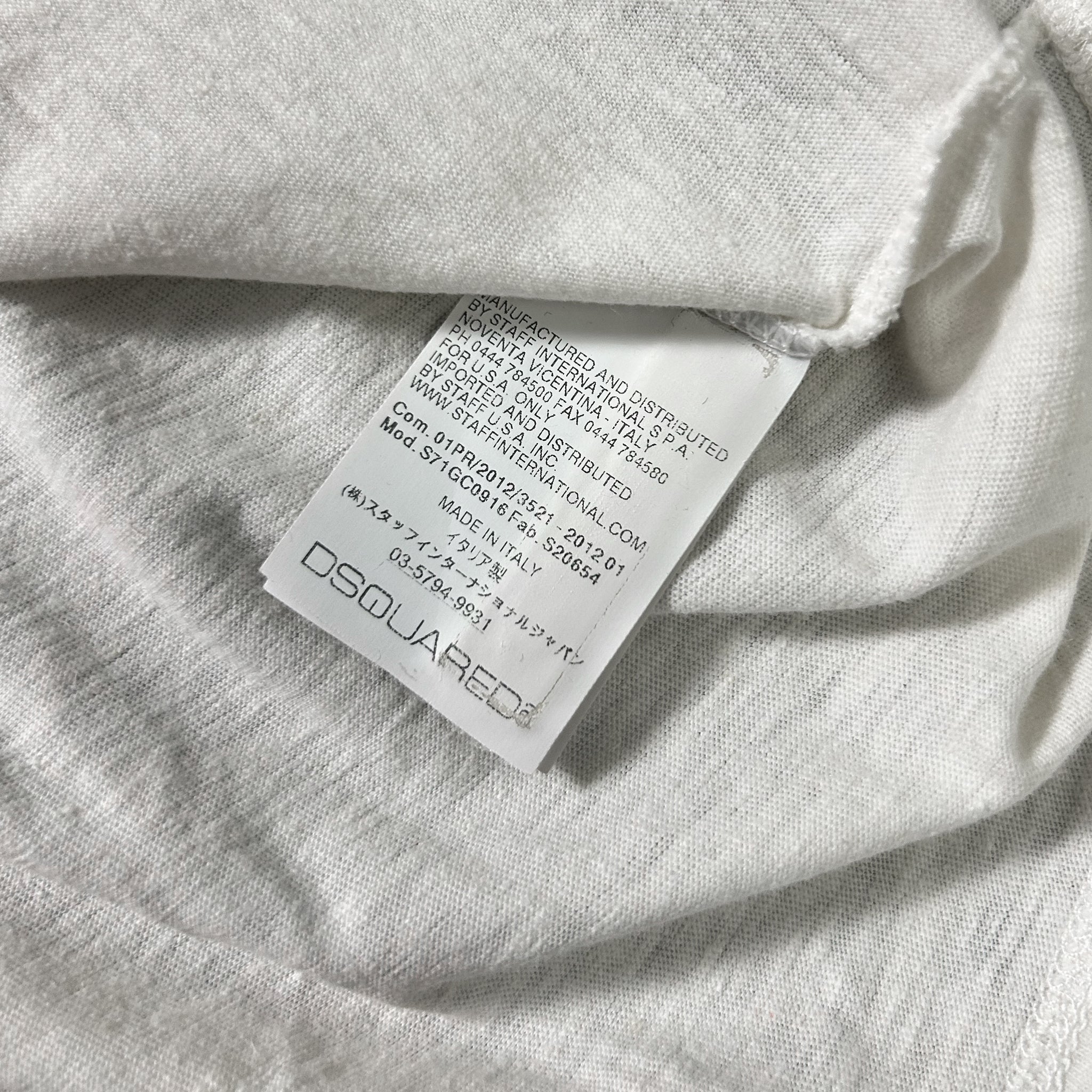 a close-up view of a white fabric, possibly a piece of clothing, with a label attached to it. The label appears to be a tag or label from a clothing brand, and it contains text in a foreign language.