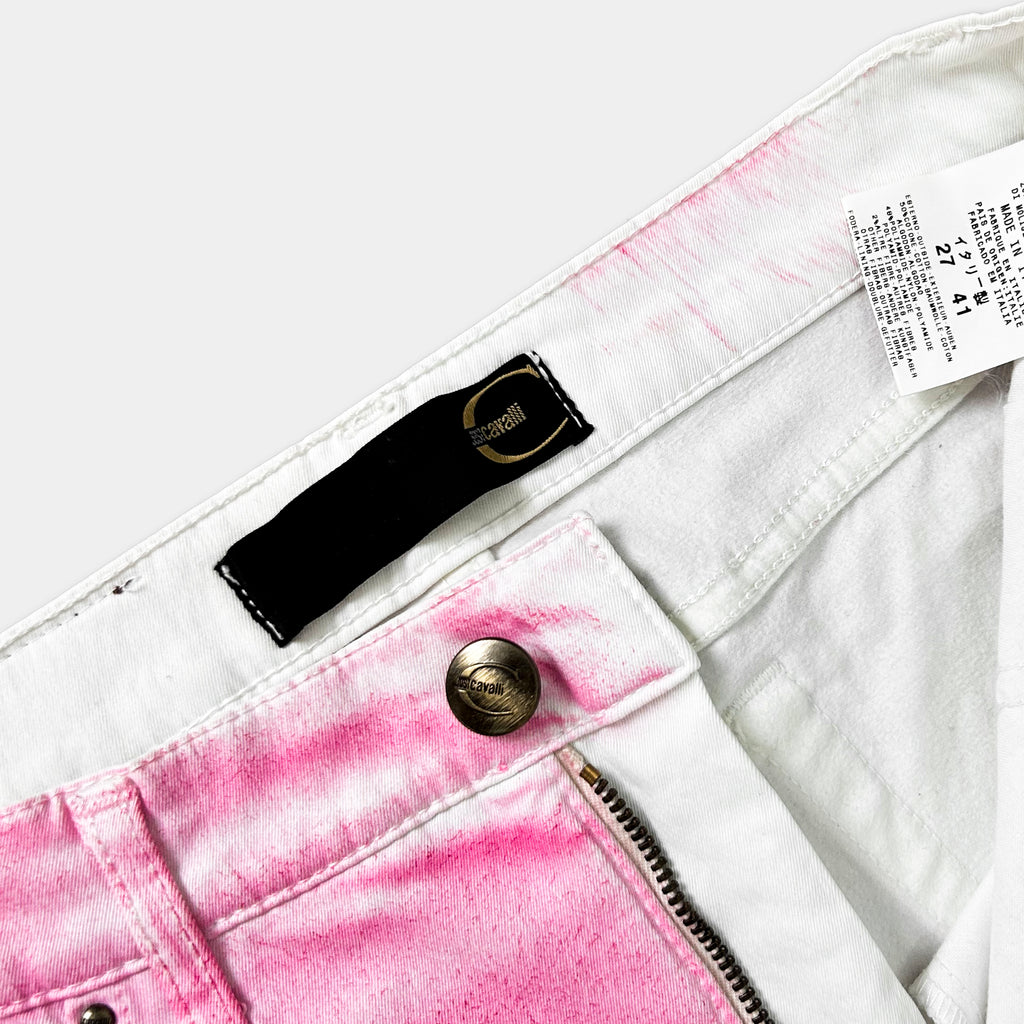 A close-up view of a pair of white jeans with a pink stain on the waistband, and a black label attached to the waistband.