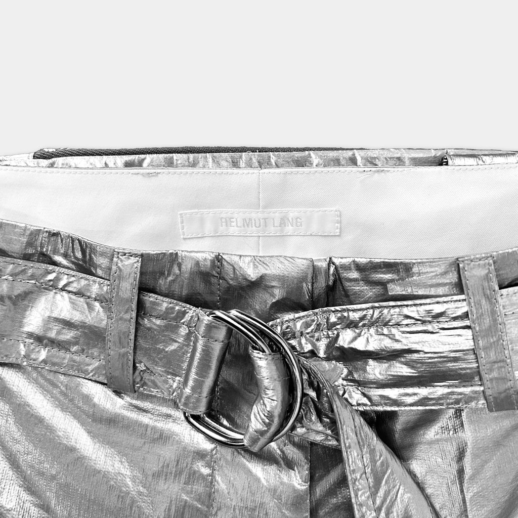A close-up view of a shiny, metallic belt with a buckle, showing the brand name "Helmut Lang" on the waistband.