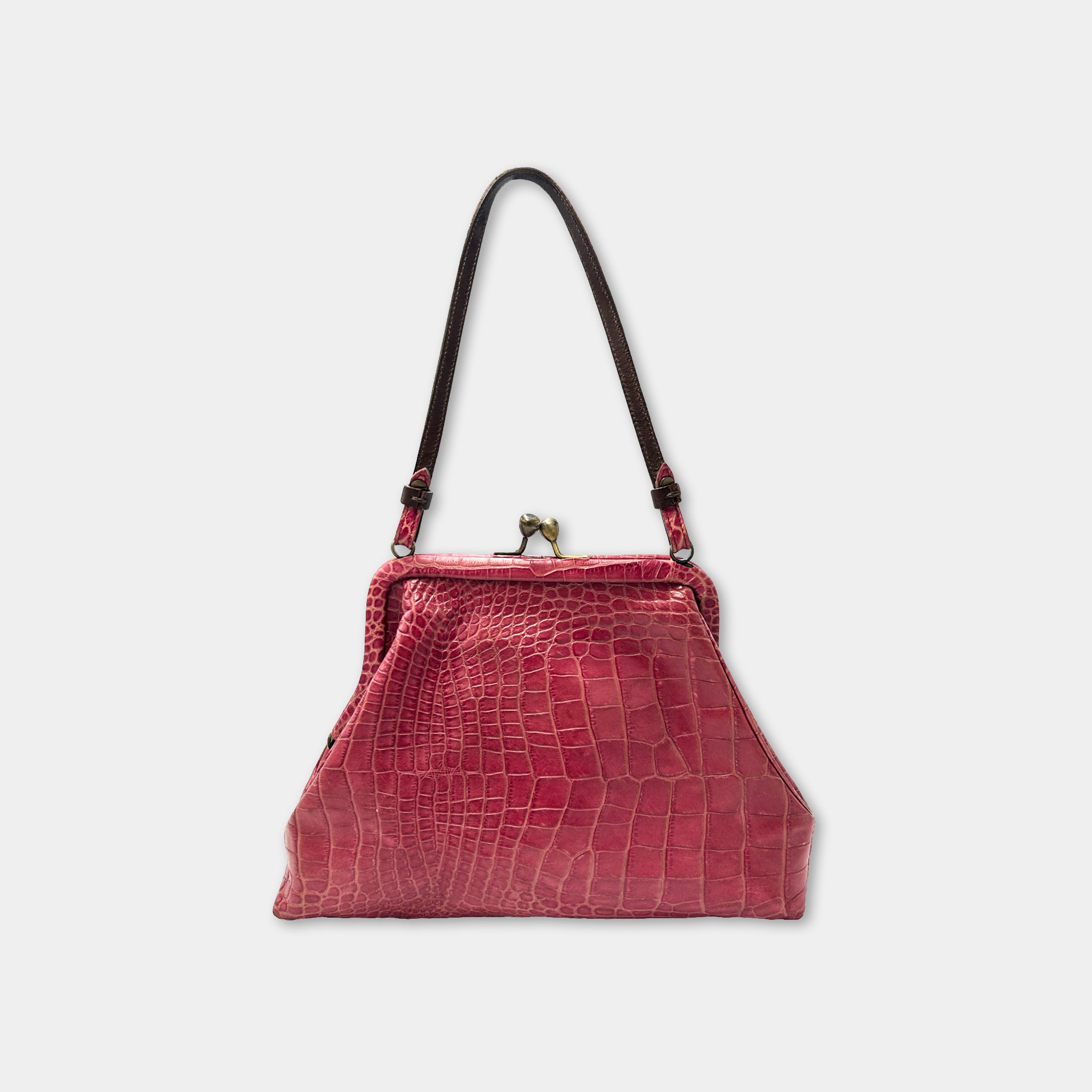 A pink leather handbag with a crocodile skin texture and a black leather strap.