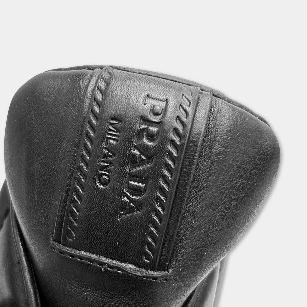 A close-up view of a black leather shoe, with the brand name "PRADA" embossed on the upper part of the shoe.