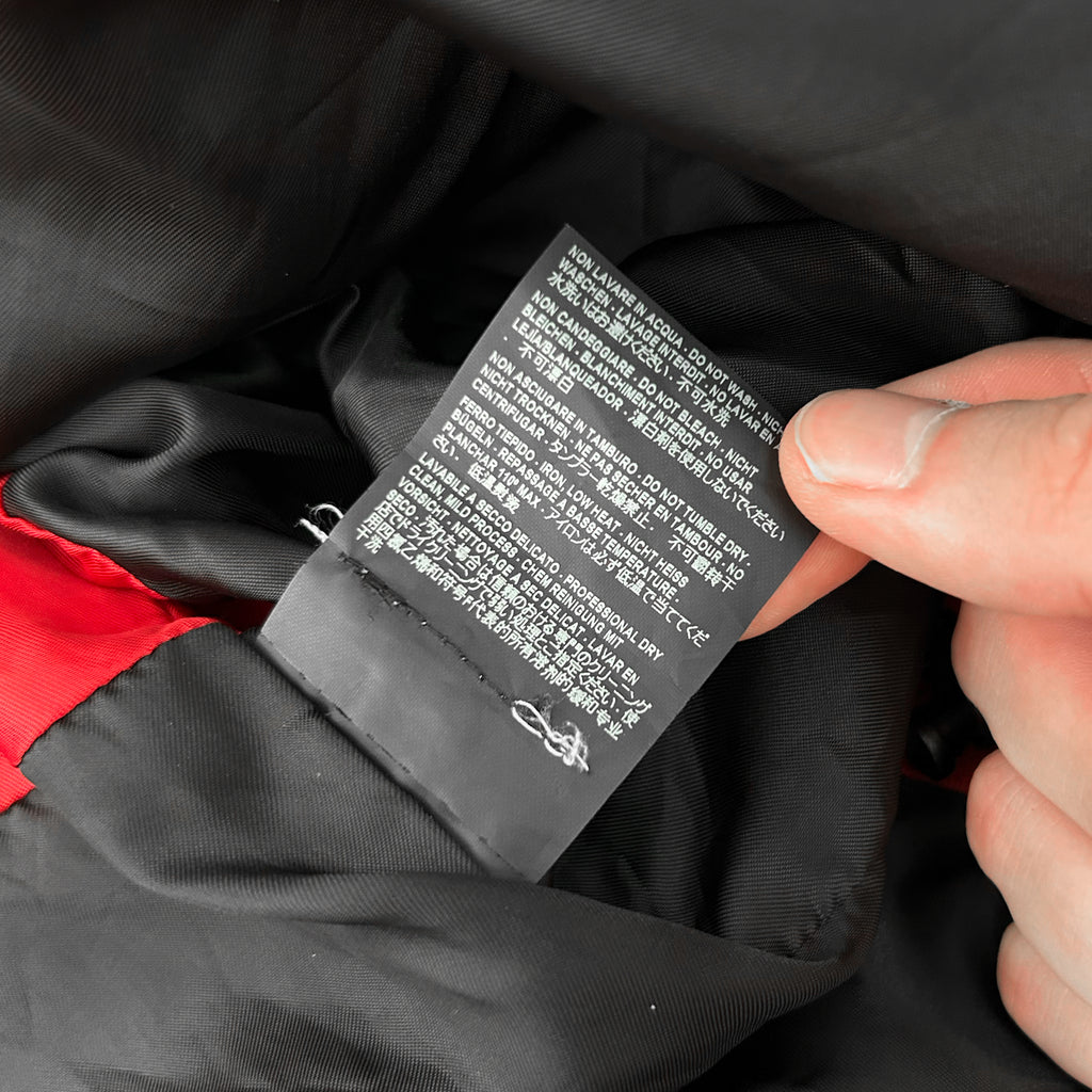 A person's hand is holding a black label with white text, which appears to be a garment label. The label contains instructions and information about the garment, such as washing and drying instructions, care labels, and other details.