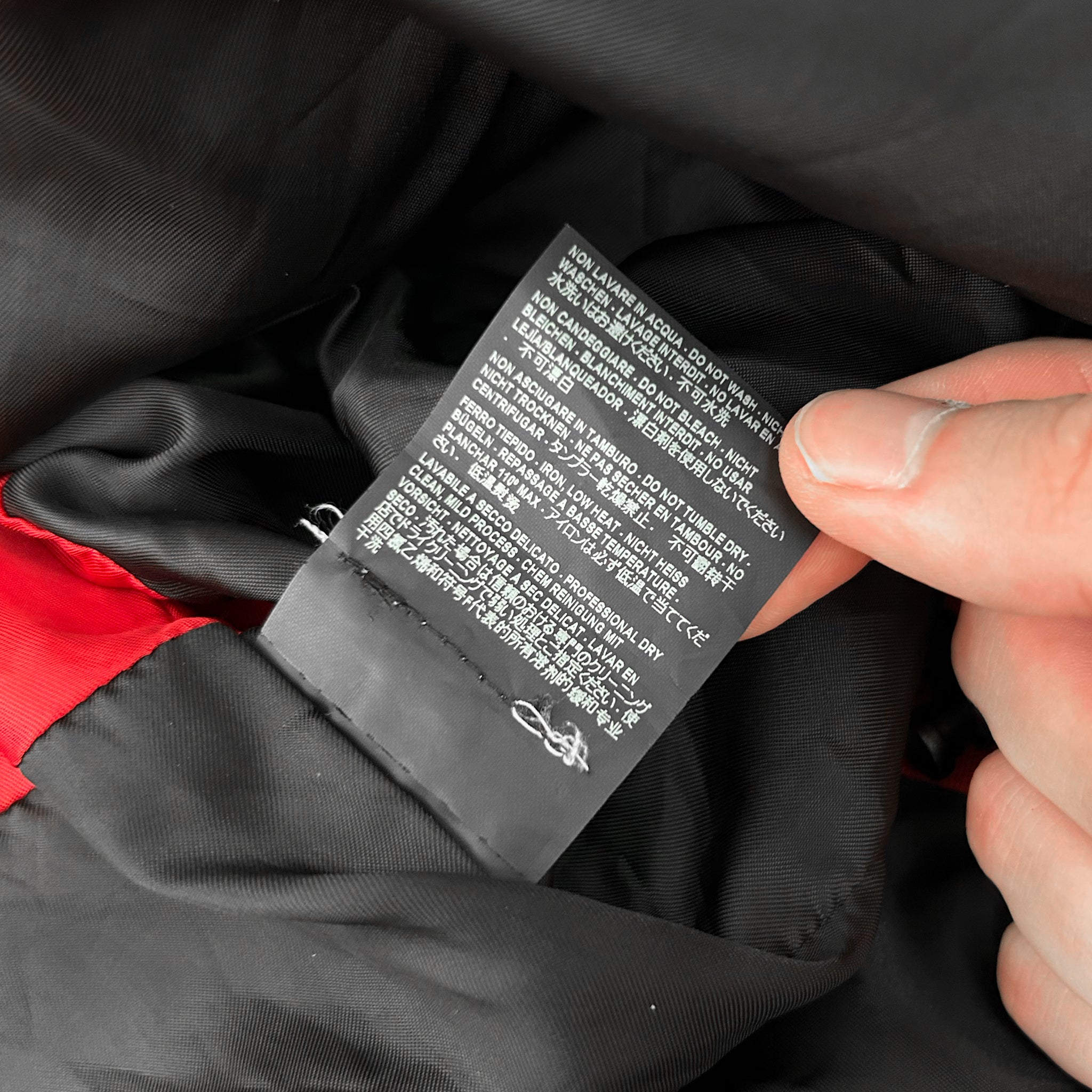 A person's hand is holding a black label with white text, which appears to be a garment label. The label contains instructions and information about the garment, such as washing and drying instructions, care labels, and other details.