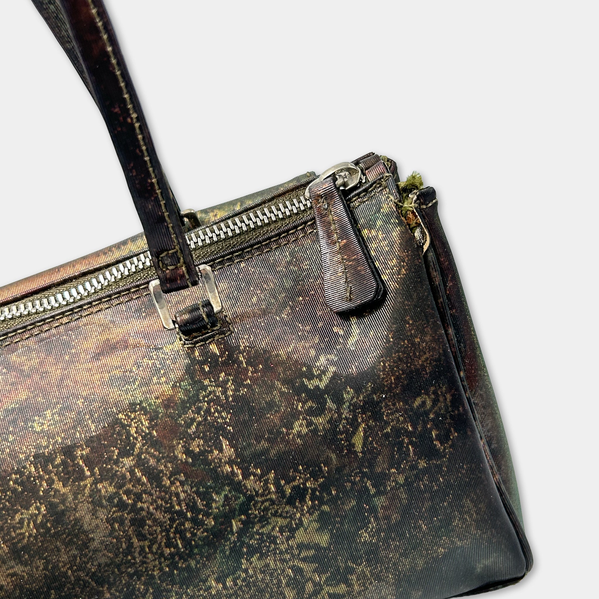 A close-up view of a dark, textured handbag with a zipper closure and a small metal clasp.