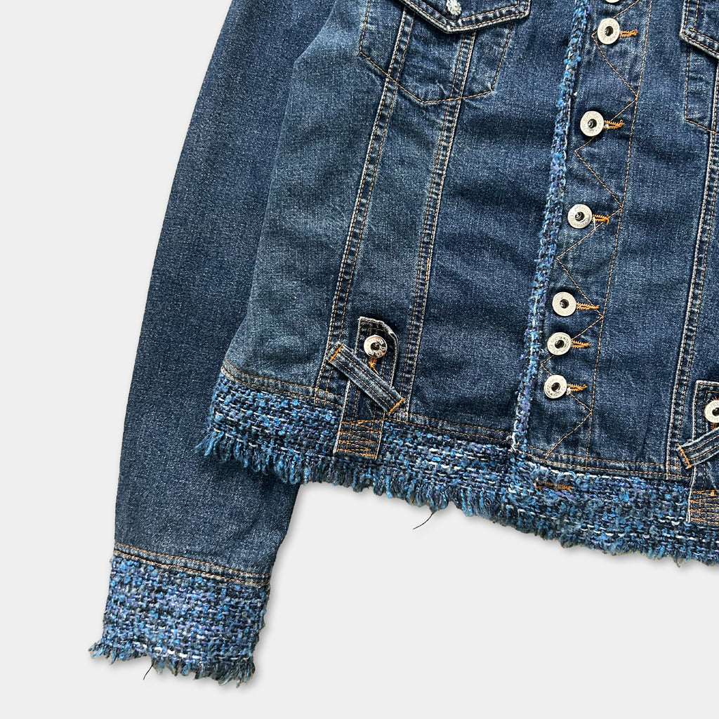 A close-up view of a denim jacket with frayed edges and a buttoned front, showcasing the details of the fabric and buttons.