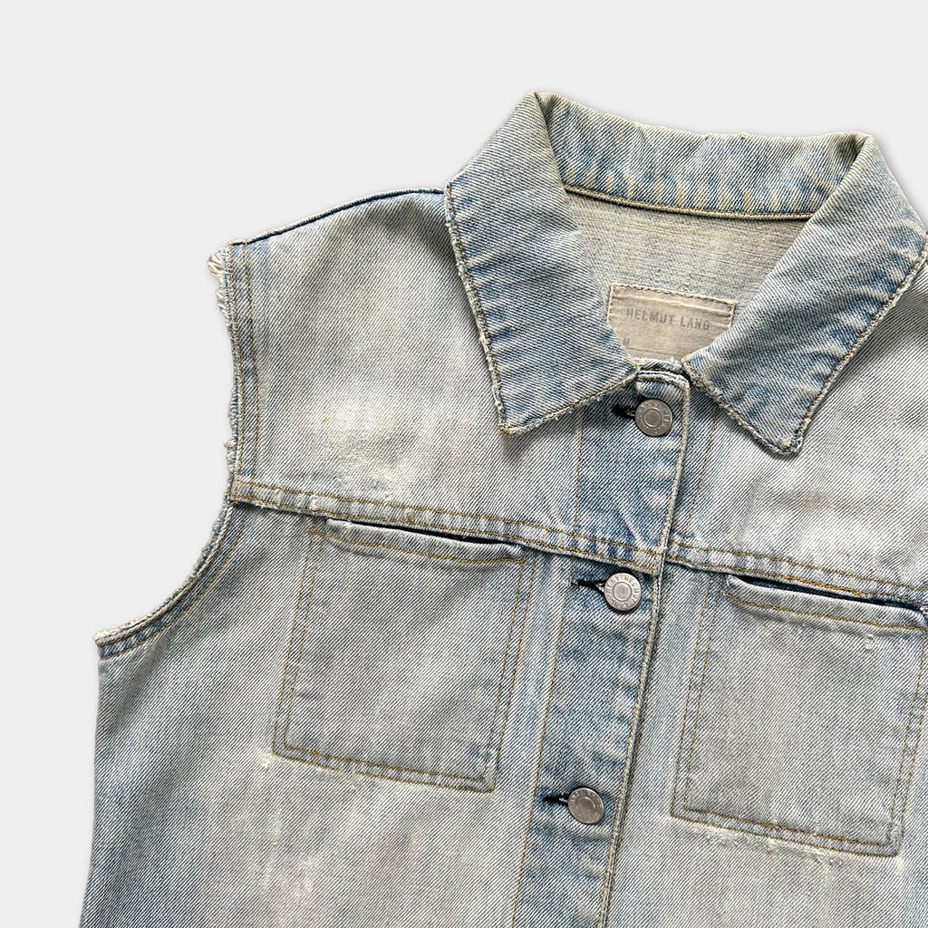 A close-up view of a denim vest with a collar and buttons, showing signs of wear and tear.