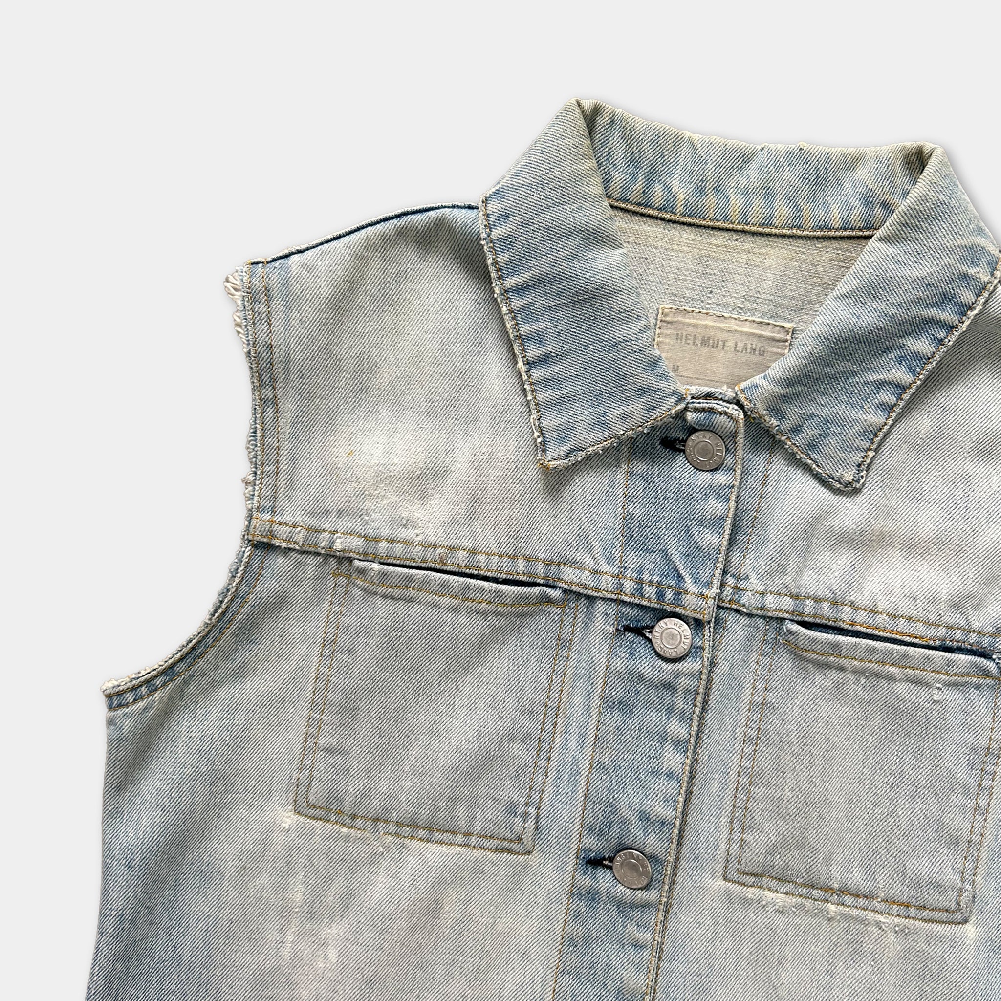 A close-up view of a denim vest with a collar and buttons, showing signs of wear and tear.