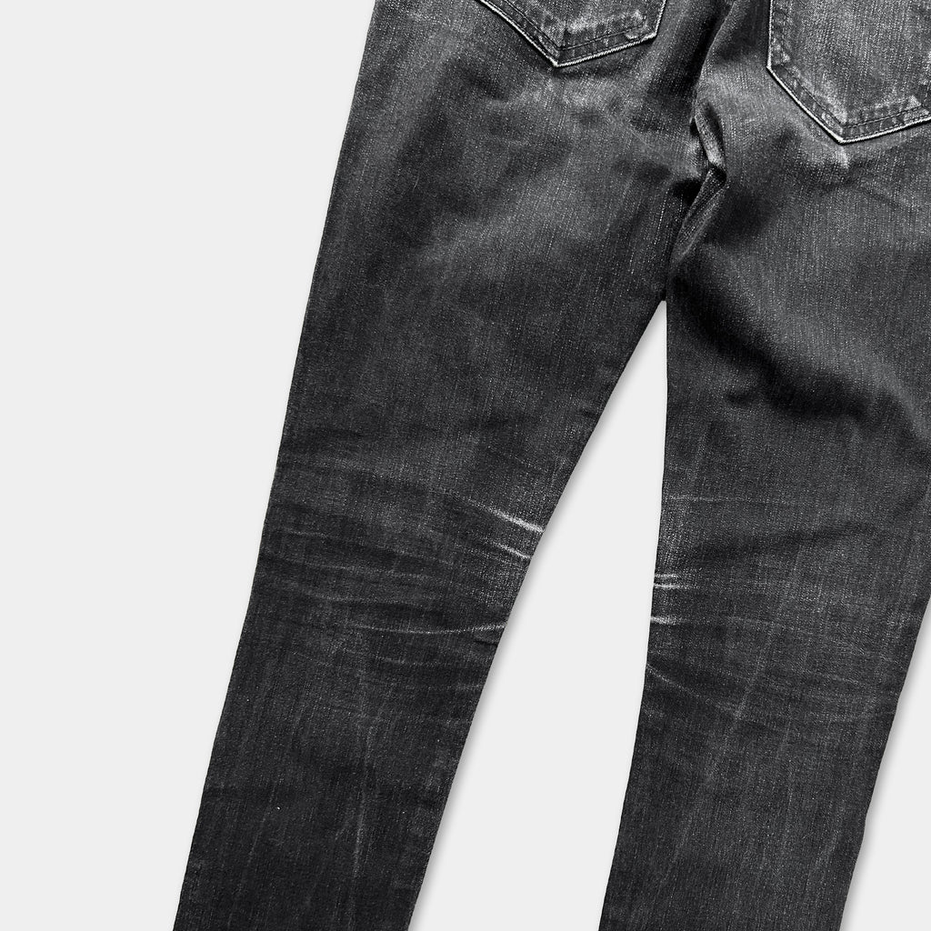 A pair of black jeans with visible signs of wear and tear, including faded and creased fabric.