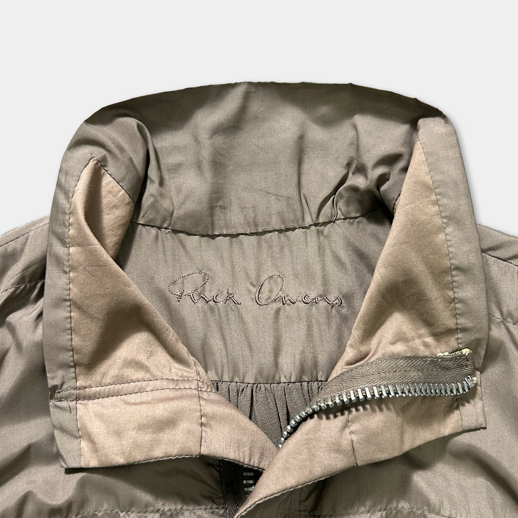 a close-up view of a brown jacket with a zipper and a small embroidered logo on the collar.