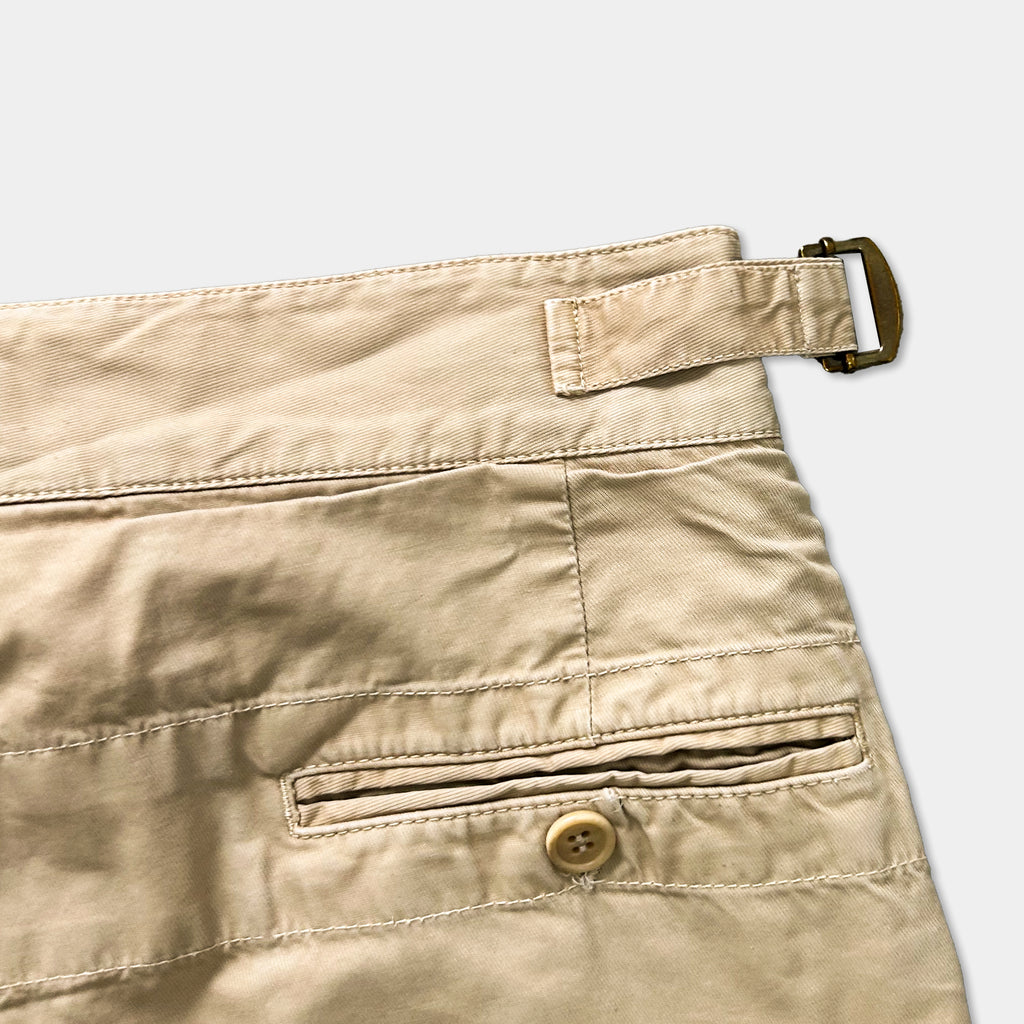 A close-up view of a pair of khaki-colored pants with a button and a buckle detail visible.