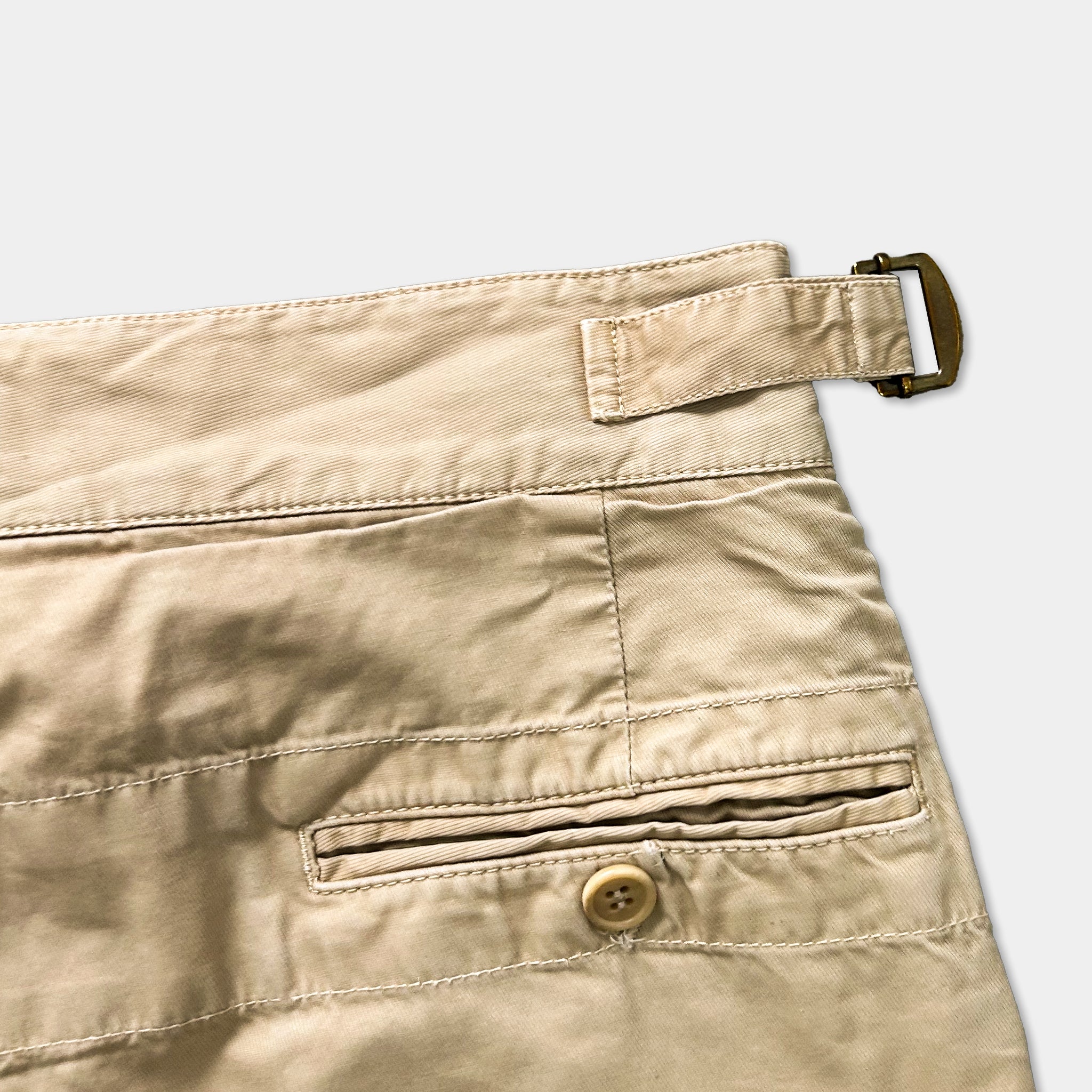 A close-up view of a pair of khaki-colored pants with a button and a buckle detail visible.