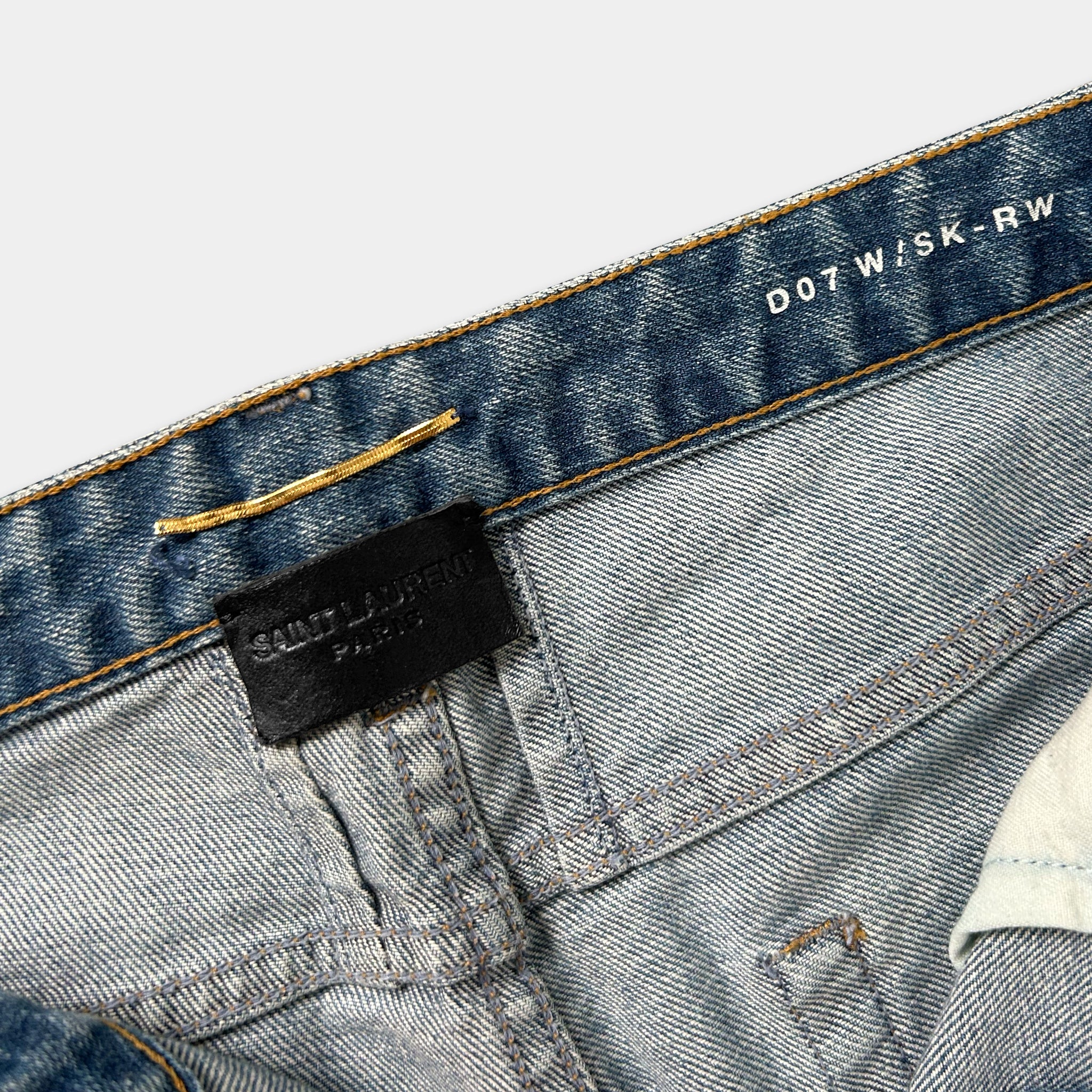 A close-up view of a pair of blue denim jeans, showing the waistband and a small black label with text.