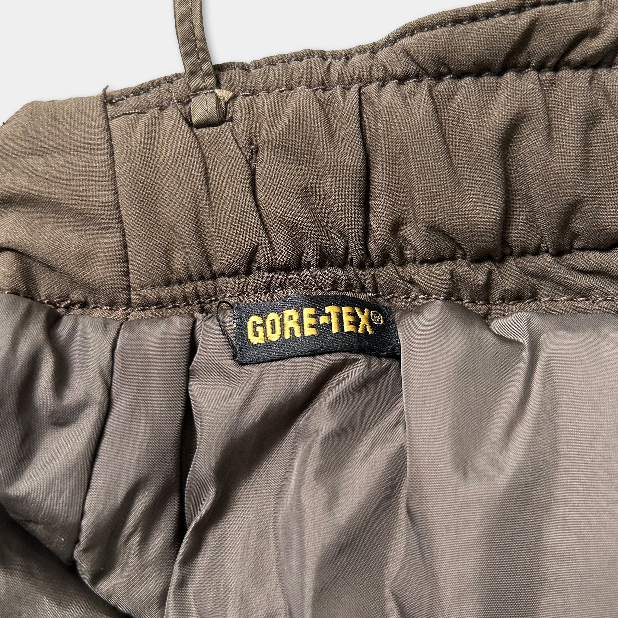 A close-up view of a pair of gray, waterproof pants with a label that reads "GORE-TEX®" on the waistband.