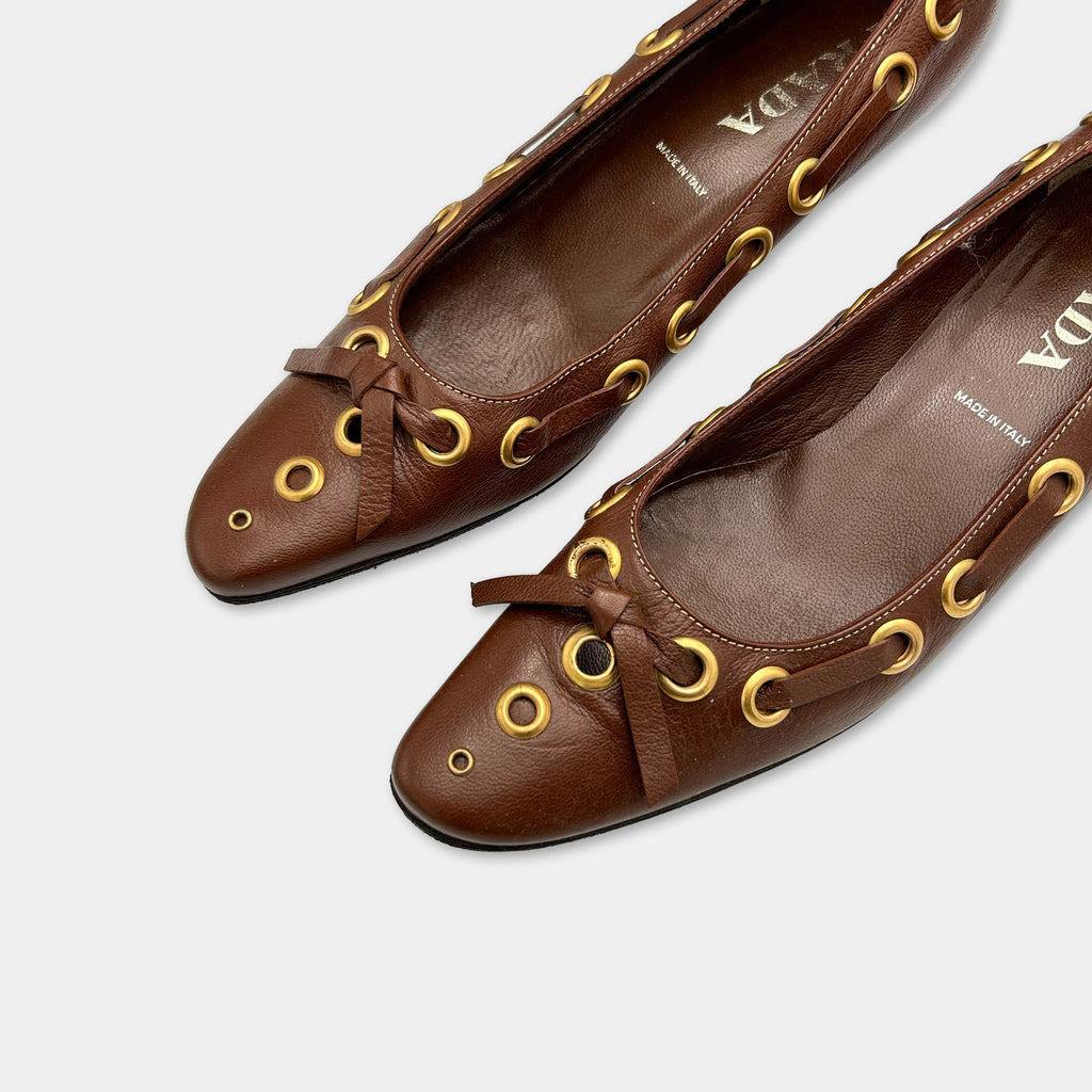 A pair of brown leather ballet flats with gold circular embellishments.