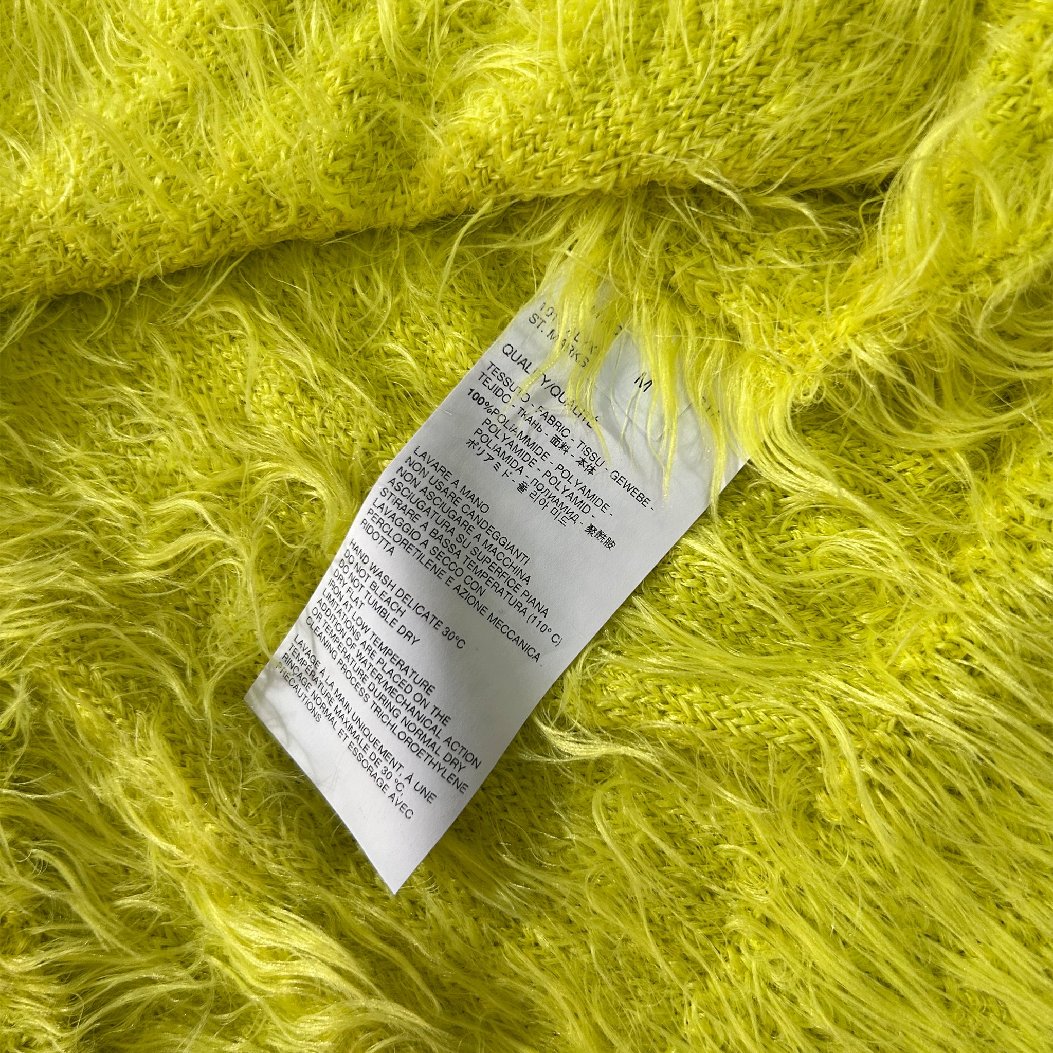a close-up of a yellow fuzzy fabric with a white label attached to it. The label contains text in a foreign language, which is not transcribed due to the language barrier.