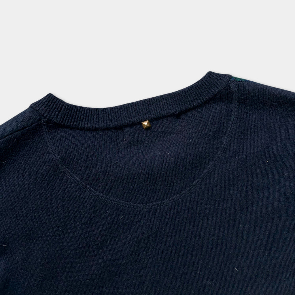 A close-up view of a navy blue sweater with a gold stud on the collar.