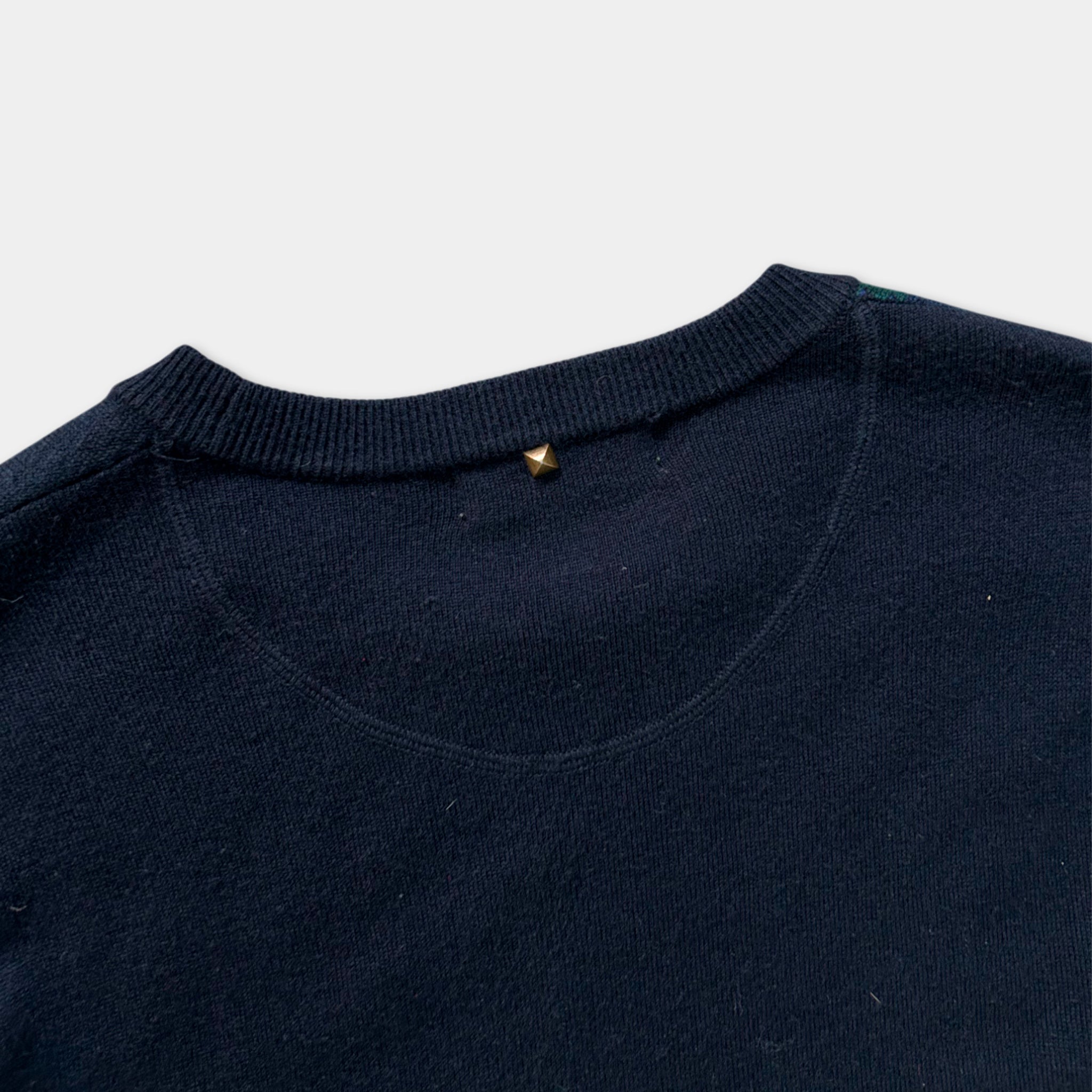 A close-up view of a navy blue sweater with a gold stud on the collar.