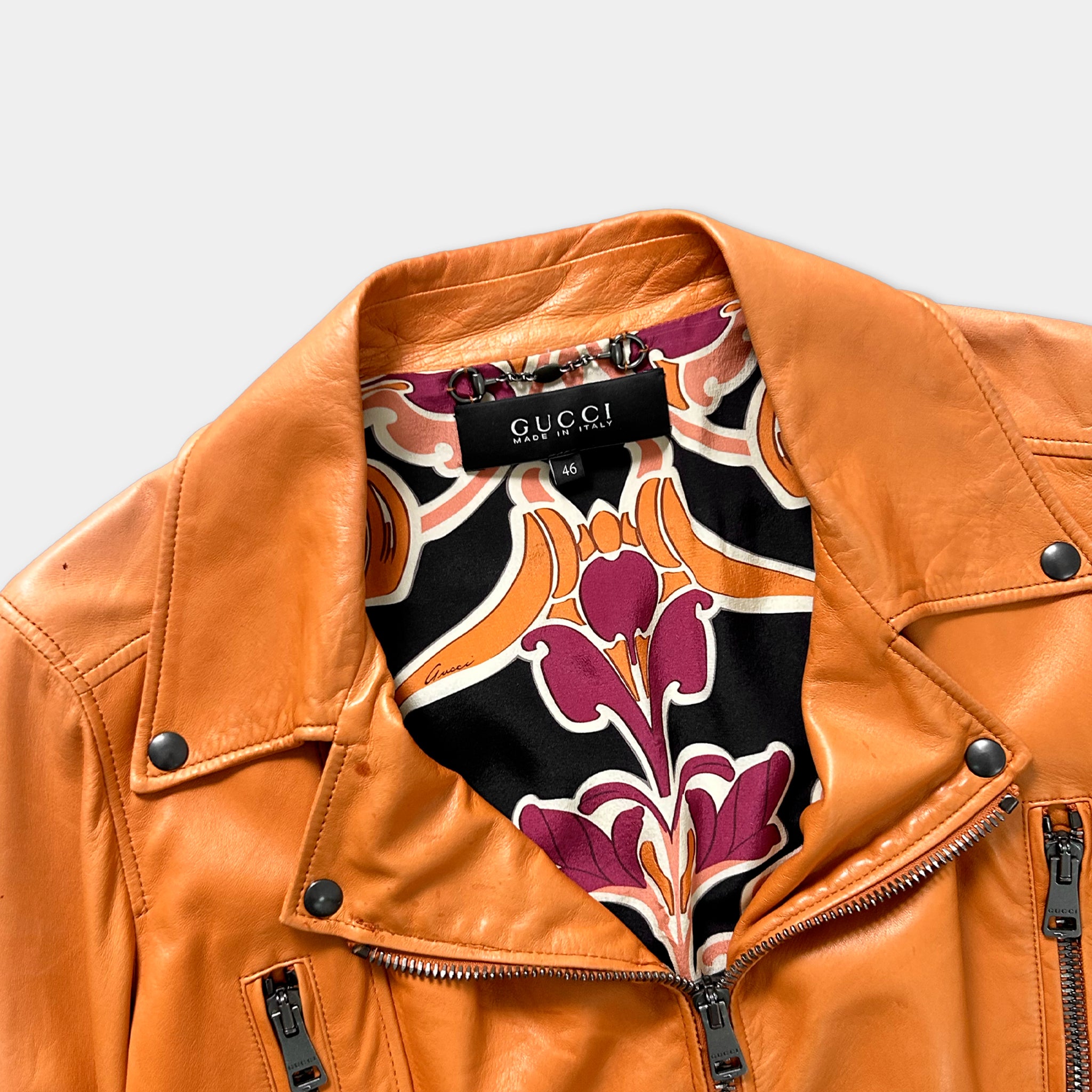 A close-up view of a bright orange Gucci leather jacket with a patterned interior lining.