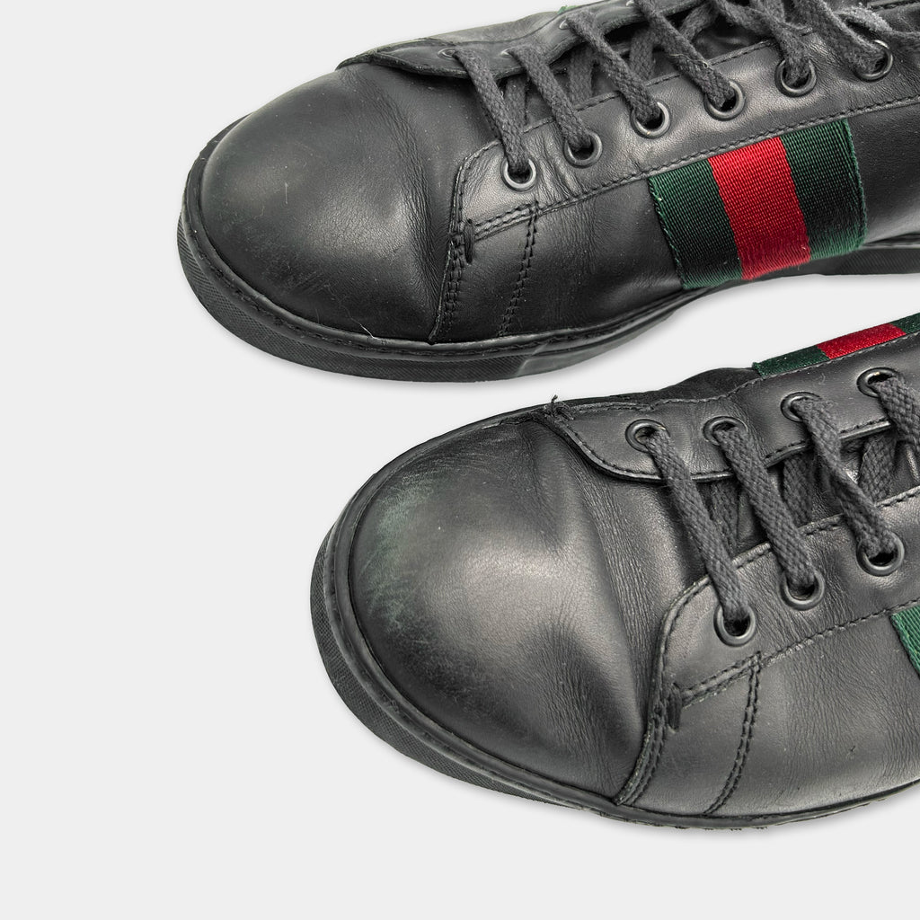 A close-up view of a pair of black leather Gucci sneakers with a distinctive red and green stripe on the side.