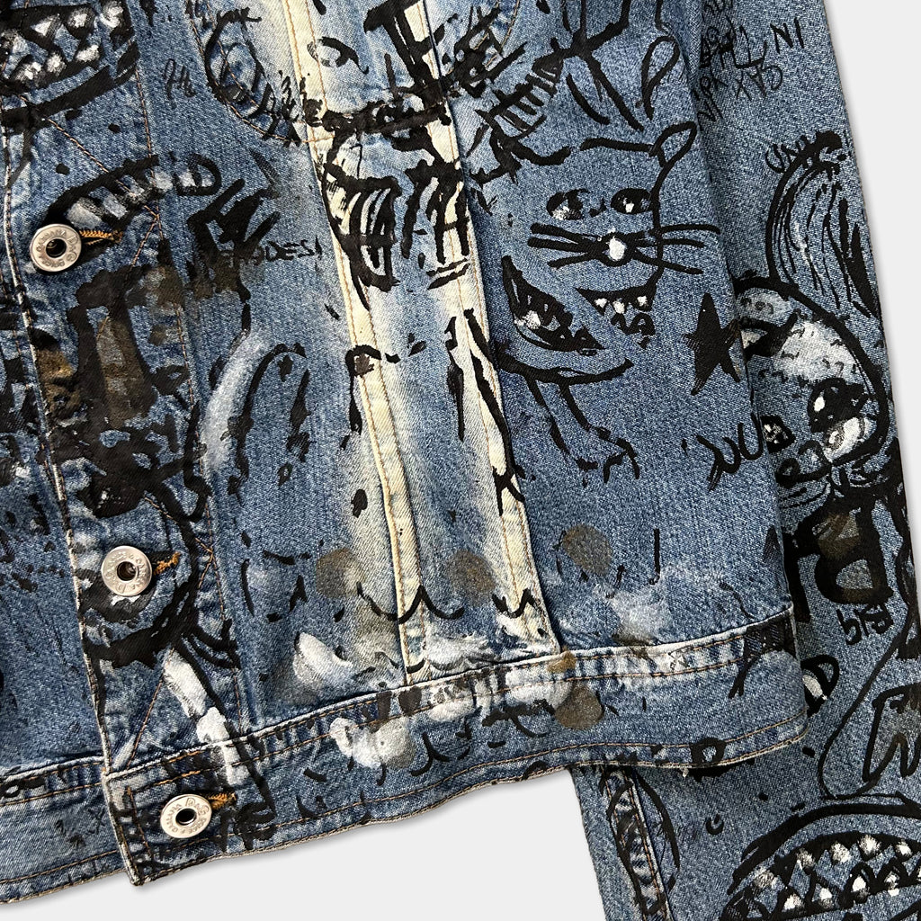 a close-up view of a denim jacket with a unique, hand-painted design featuring various cartoon-like characters and patterns.