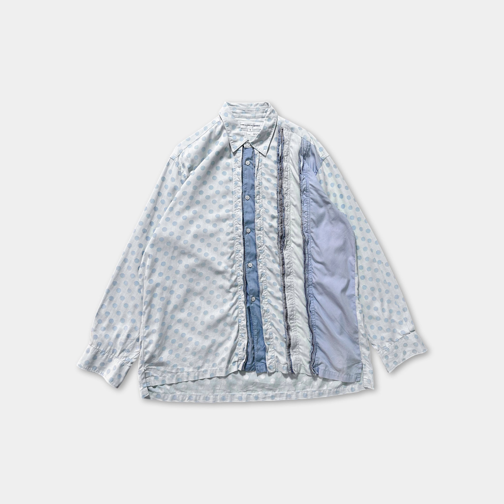 a white shirt with blue polka dots, featuring a button-down front and a folded sleeve.