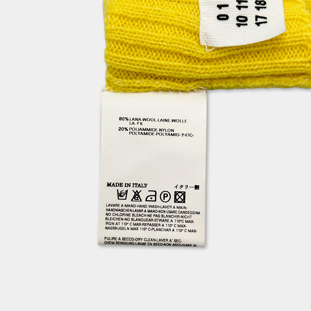 a yellow knitted garment with a white label attached to it. The label provides information about the garment, including details about the material and care instructions.