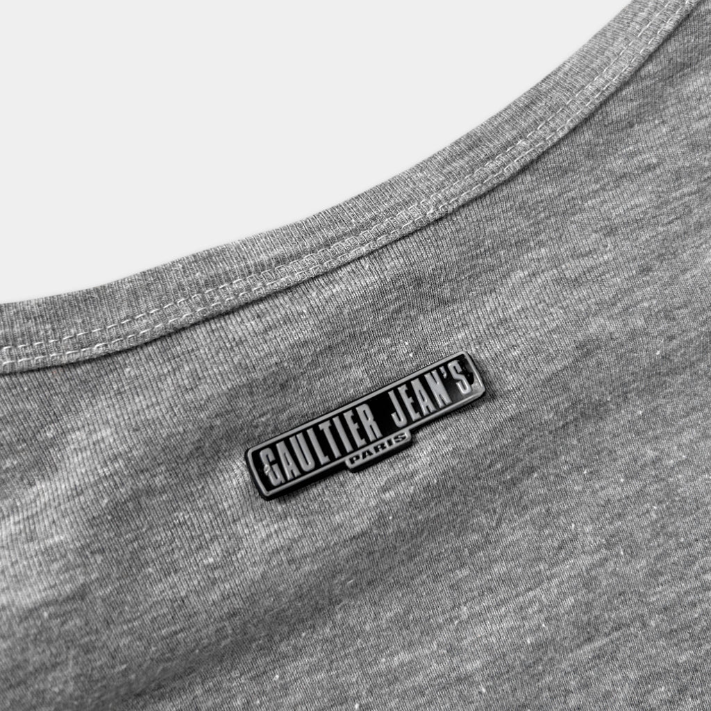 A close-up view of a grey fabric, possibly a shirt or blouse, with a metal or plastic label or patch on the back.