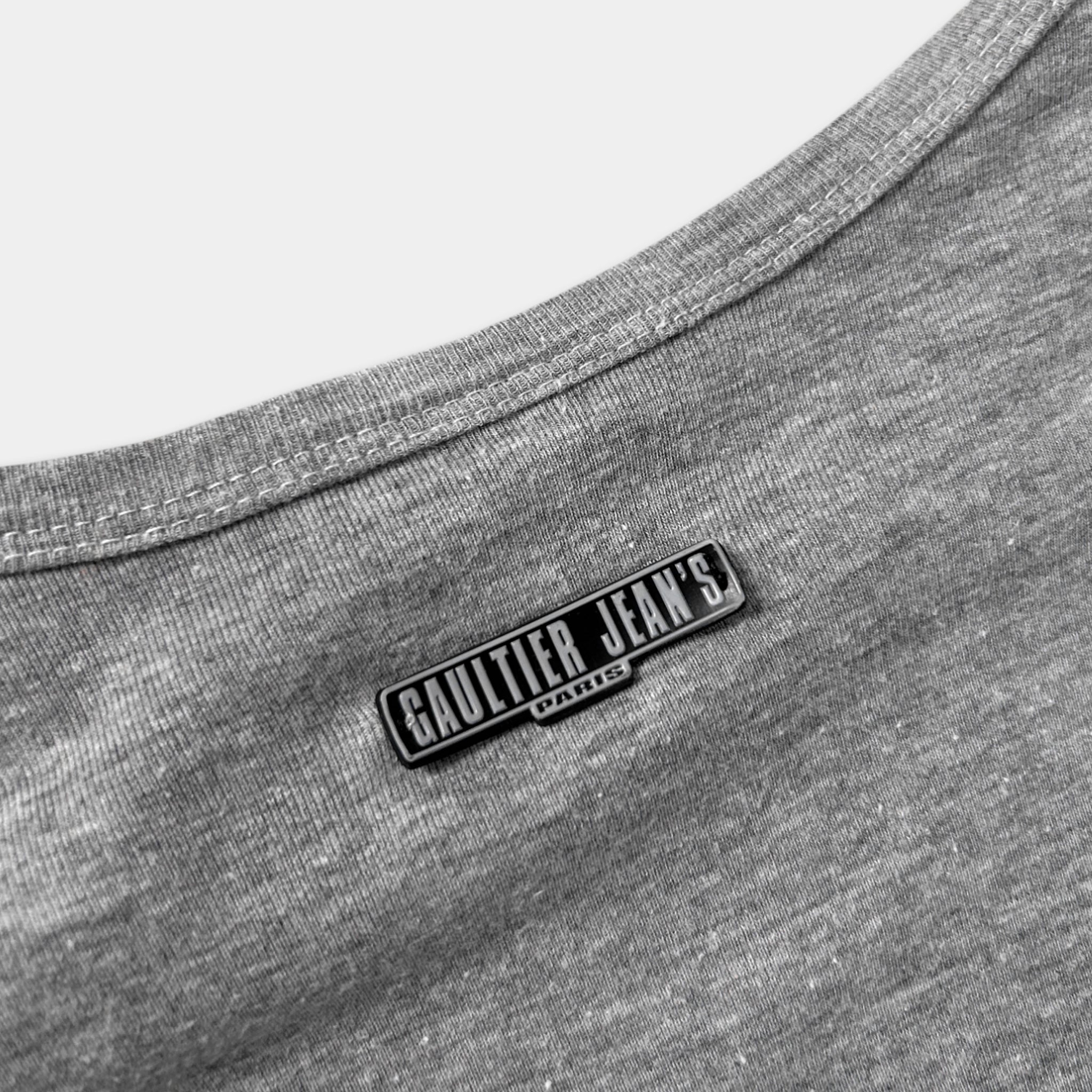 A close-up view of a grey fabric, possibly a shirt or blouse, with a metal or plastic label or patch on the back.