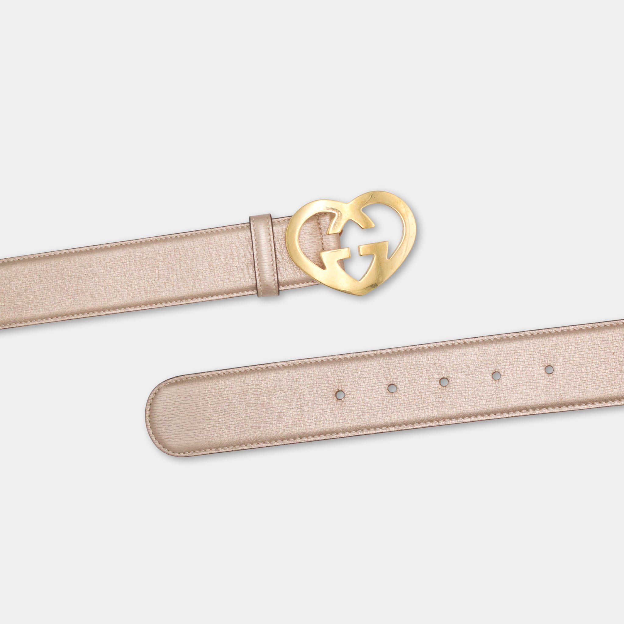 A beige leather belt with a gold buckle featuring a heart-shaped design.