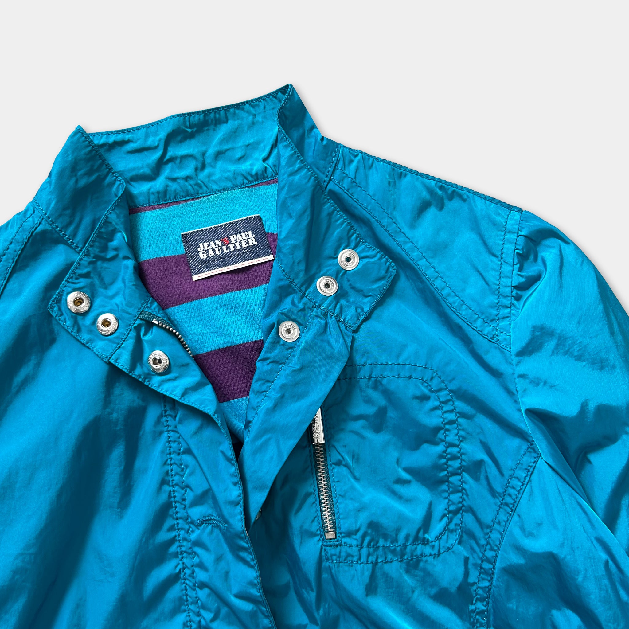 A close-up view of a bright blue jacket with a zipper and a label on the collar.
