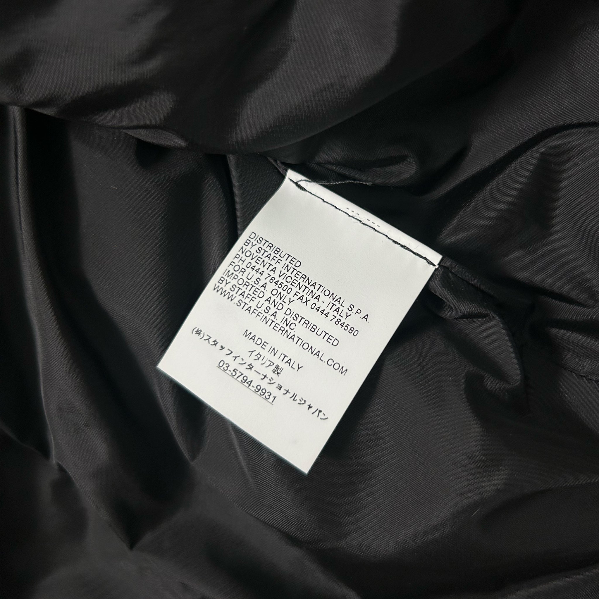 a close-up view of a black fabric, possibly a piece of clothing or a textile. The fabric appears to be made of a shiny material, possibly silk or satin. There is a white label attached to the fabric, which contains text in a foreign language. The label appears to be a product description or information related to the fabric, such as its origin, material, or care instructions. The image does not contain any other objects or text, and the overall scene is focused on the fabric and the label.