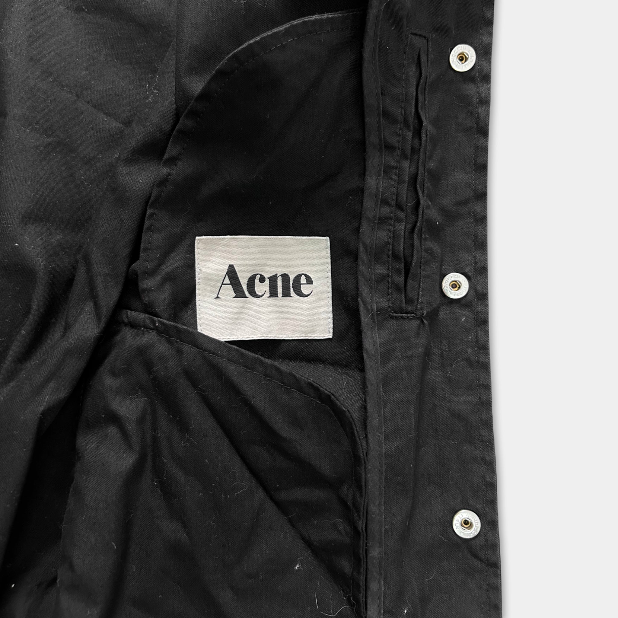 a close-up view of a black jacket with a label that reads "Acne" on the pocket.